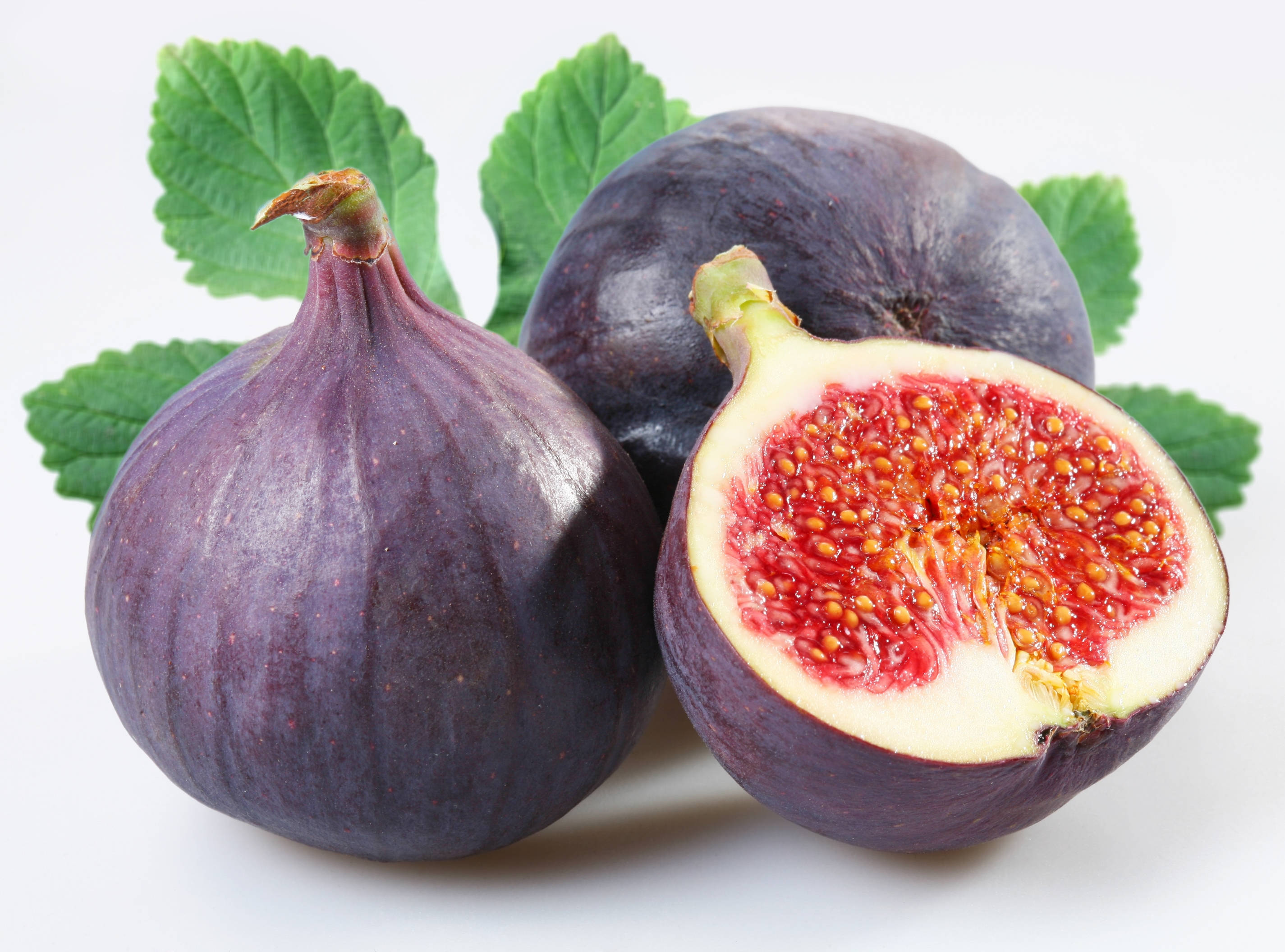 Fruit 桌布 壁紙 — 三個成熟的紫色無花果，其中一個切開，露出多汁的紅色種子和奶油般的果肉，襯著綠葉，白色背景。