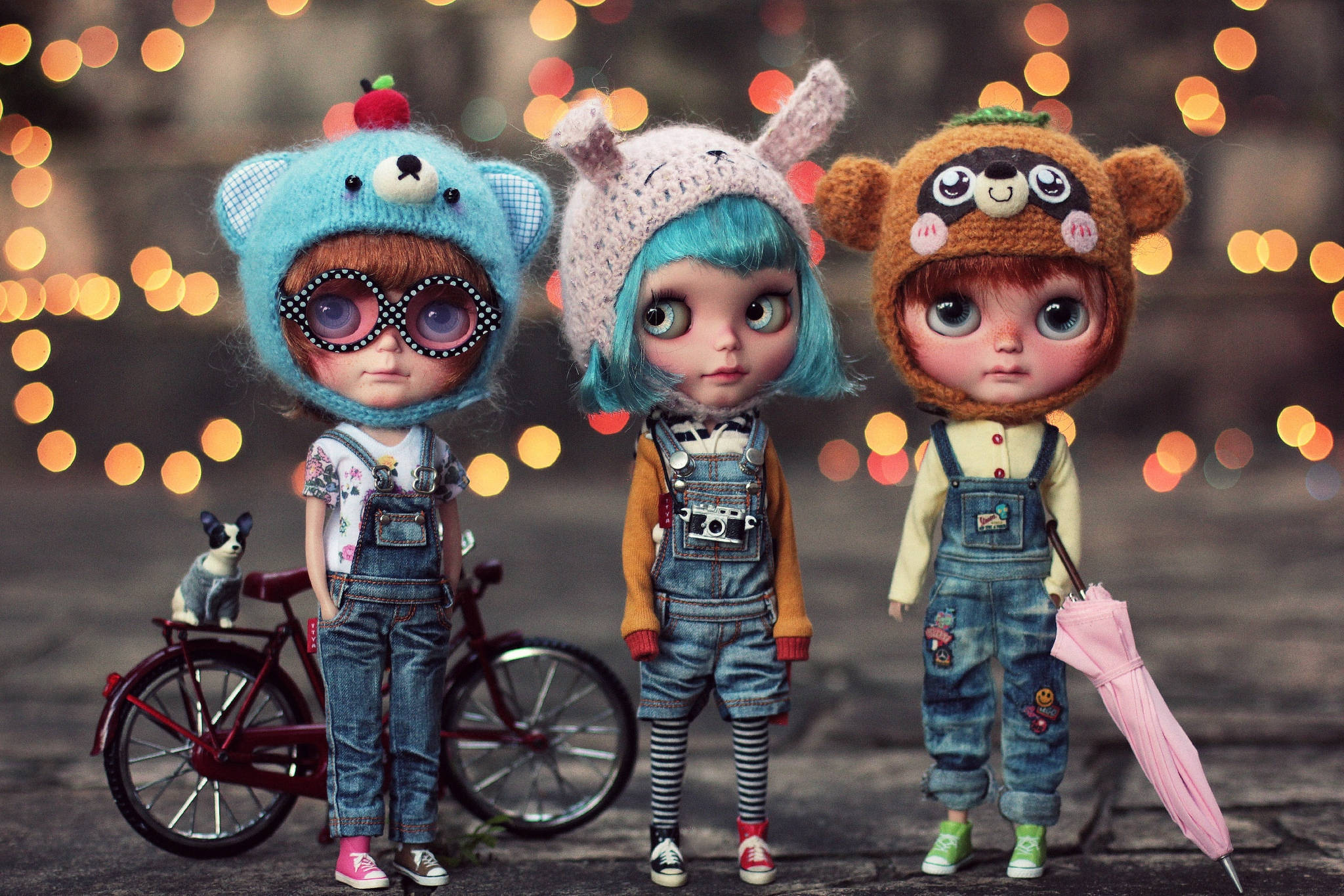 3 Best Friends 桌布 壁紙 — 三個戴動物帽和穿吊帶褲的Blythe娃娃，旁邊有一輛紅色腳踏車和一隻貓，背景是溫暖的散景燈光。
