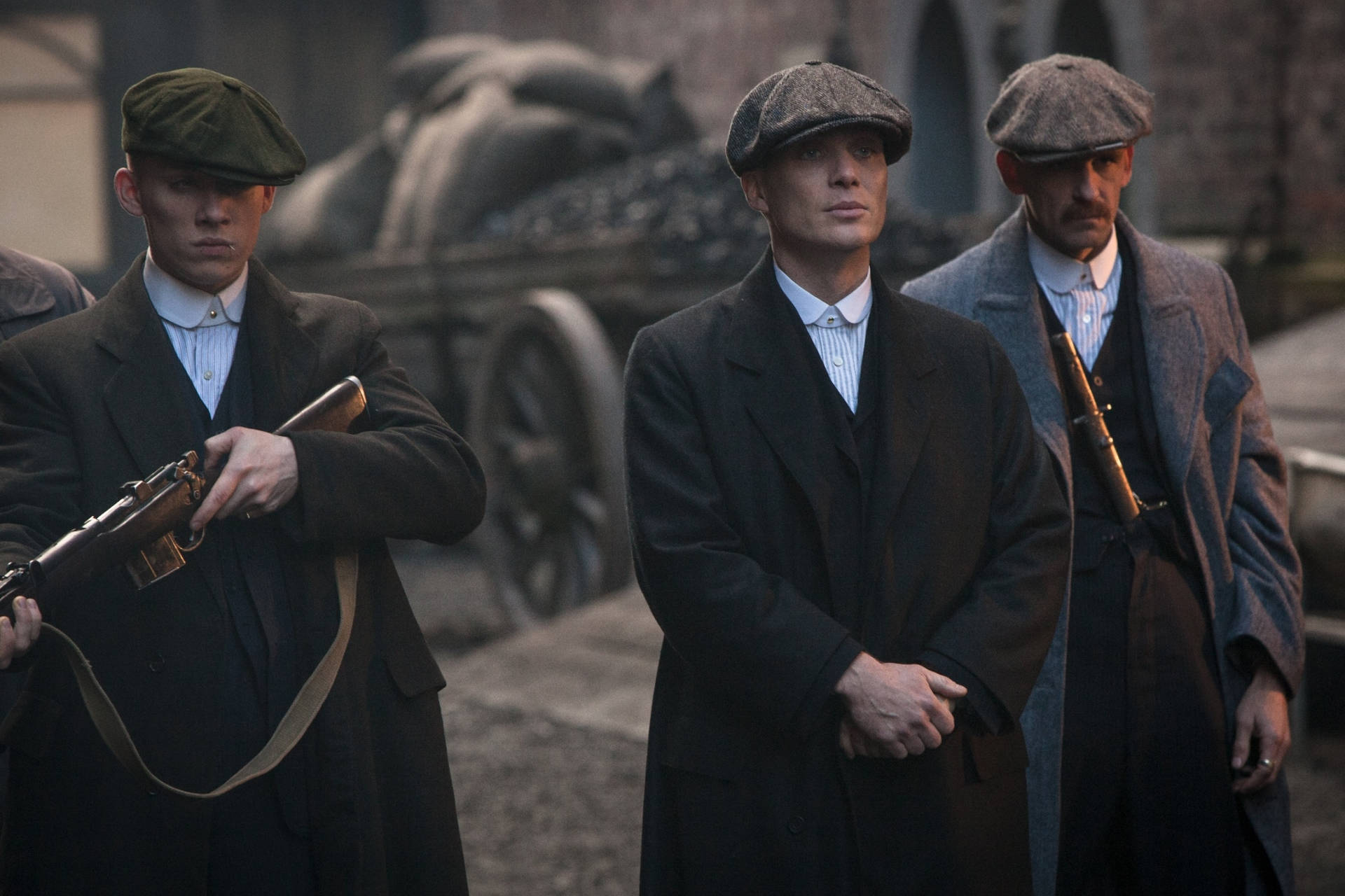 三個身穿1920年代黑幫服裝的男人在石巷中持步槍。 — Peaky Blinders 壁紙