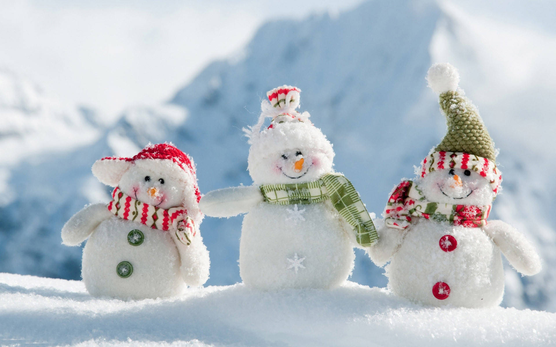 酷炫可爱 桌布 壁紙 — 三個戴著圍巾和帽子的快樂雪人，在明亮的陽光下手牽手站在白雪皚皚的山坡上。