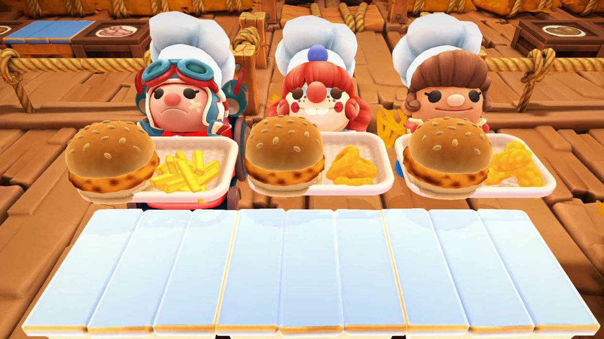 Overcooked 桌布 壁紙 — 三個戴著廚師帽的卡通廚師在木甲板上用藍色托盤供應漢堡和薯條。