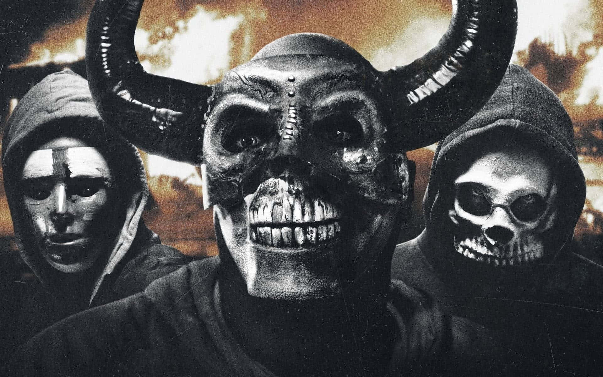 Halloween Masks 桌布 壁紙 — 三個戴連帽衫的人物戴著怪誕面具——一個有角和縫合的嘴，另一個有骷髏設計，背景是火熱的末日景象。