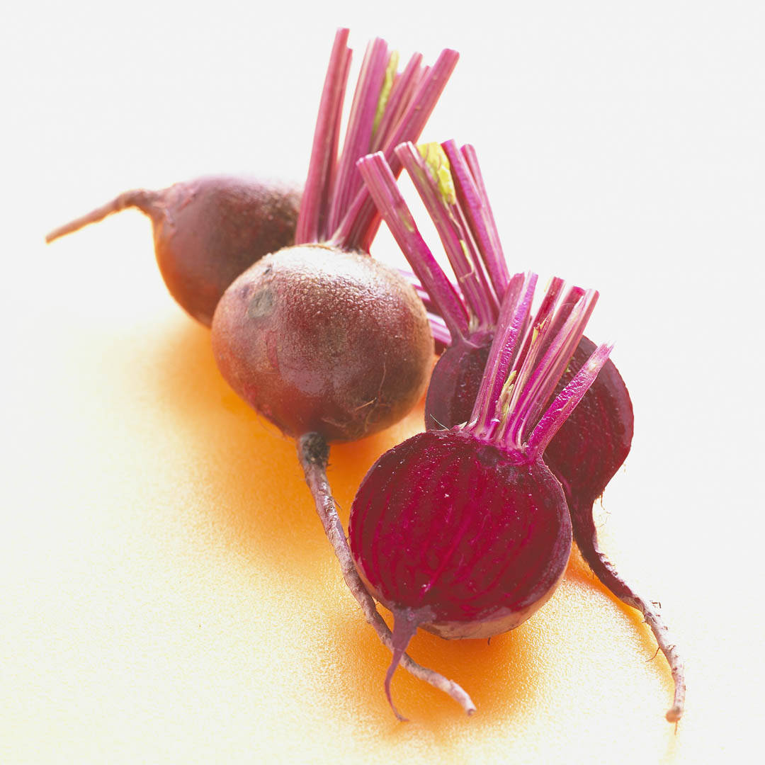 beetroot 桌布 壁紙 — 三個新鮮的甜菜根帶有充滿活力的紫色莖，放在溫暖的黃色表面上，背景是明亮的白色。