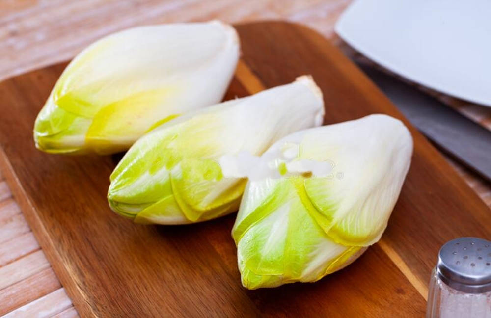 Food Photography 桌布 壁紙 — 三個新鮮的菊苣頭，帶有淡綠色和白色的葉子，放在木製砧板上，旁邊有鹽罐和刀。