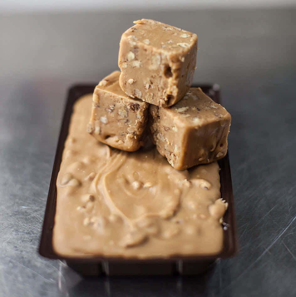 Penuche Fudge 桌布 壁紙 — 三個方形花生醬軟糖方塊堆疊在一個奶油軟糖托盤上，置於拉絲金屬表面。
