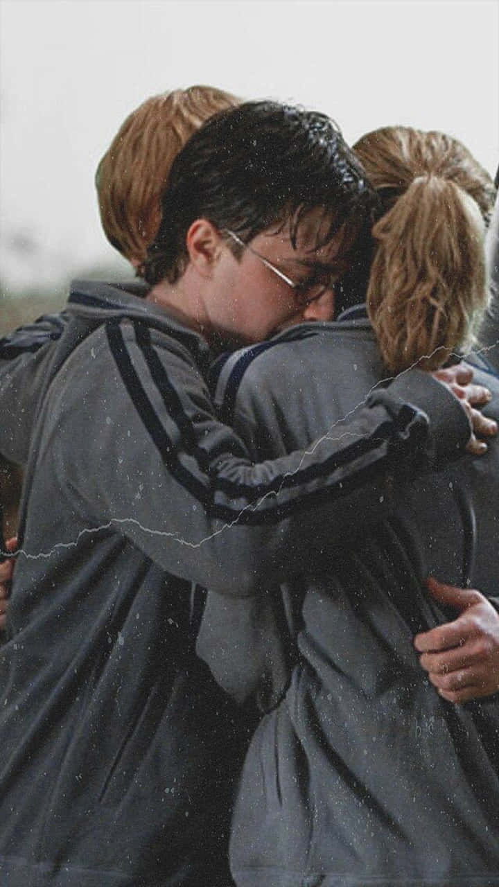 Ron Weasley 桌布 壁紙 — 三個朋友在雪景中緊緊擁抱，他們的呼吸清晰可見，分享著安慰與溫暖的時刻。