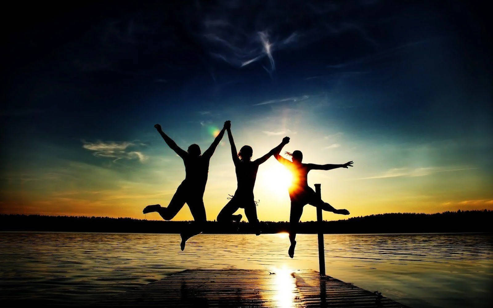 3 Best Friends 桌布 壁紙 — 三個歡樂的剪影在日落時從碼頭躍起，在平靜的水面上投下長長的影子，天空壯麗。
