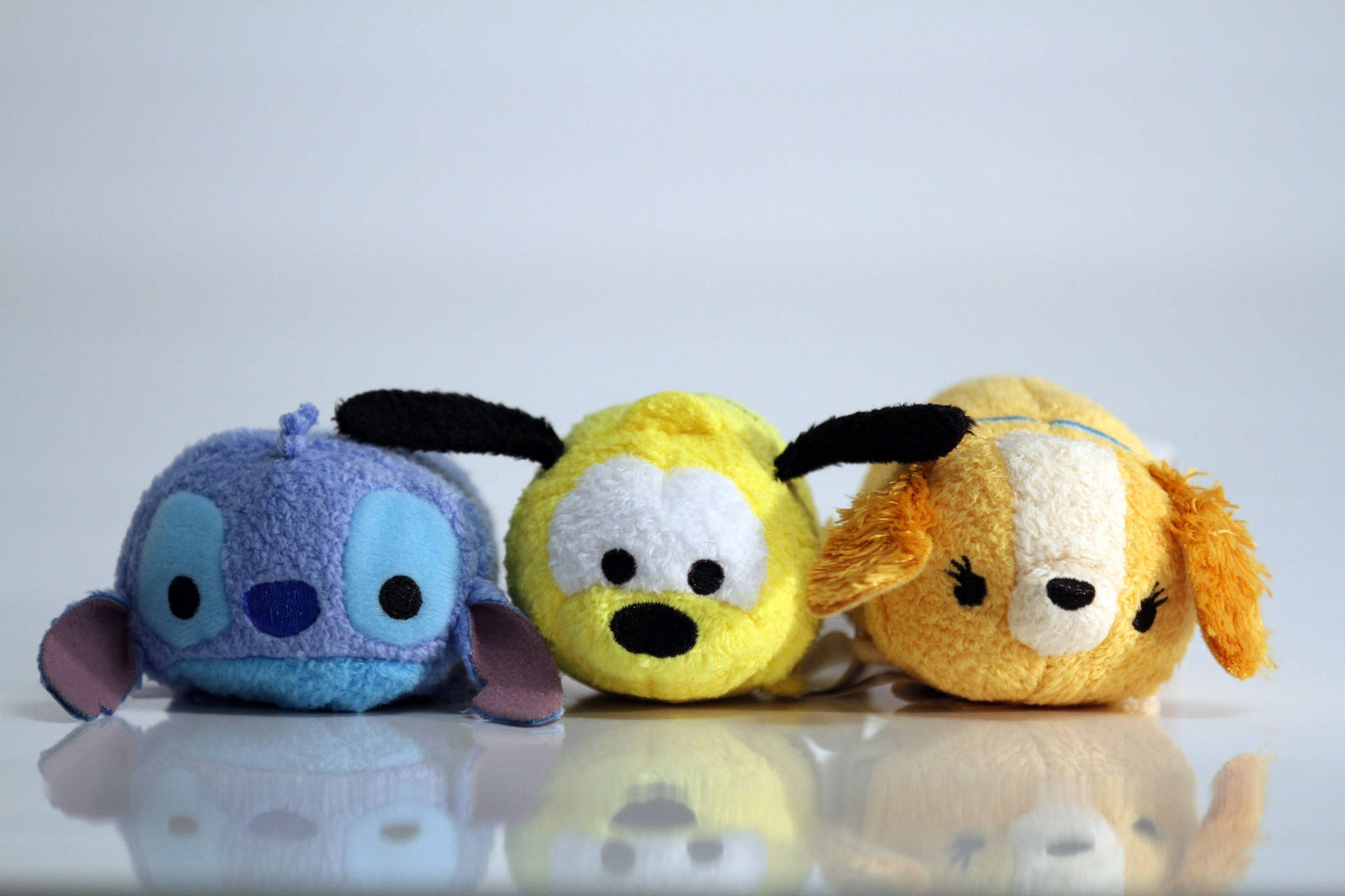 三個藍色、黃色和橙色的迪士尼Tsum Tsum毛絨玩具在反光表面上。 — Tsum tsum 壁紙