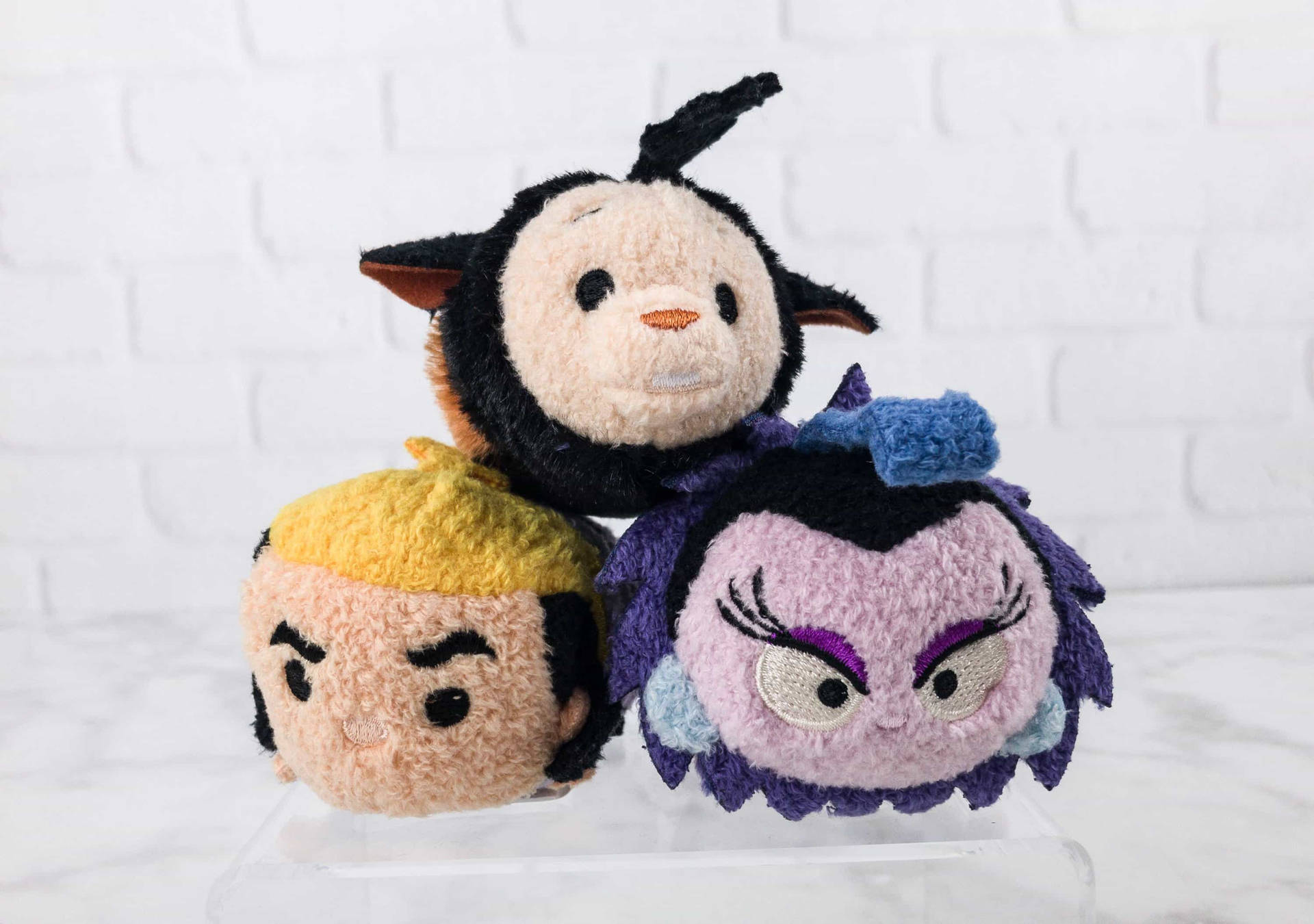 三個迪士尼 Tsum Tsum 毛絨玩具，擁有獨特面孔，排列在透明架上。 — Tsum tsum 壁紙