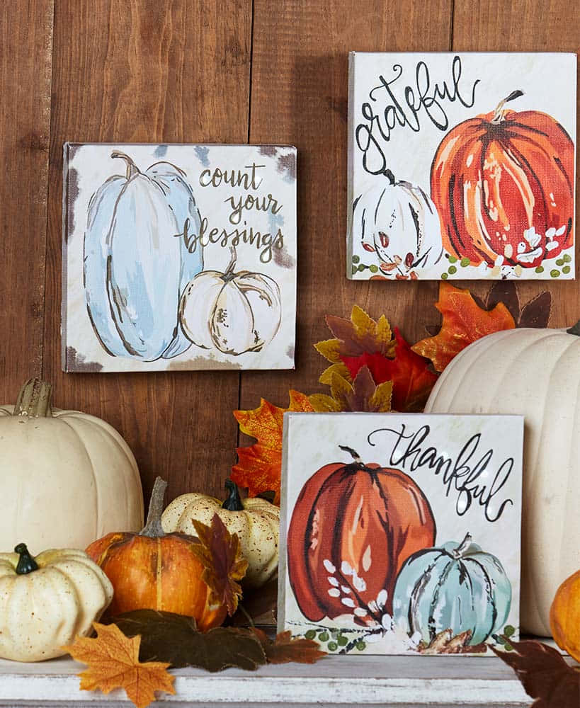 Fall Thanksgiving 桌布 壁紙 — 三個水彩南瓜畫在畫布上，感恩語句點綴其中，與真實的秋葉和南瓜一起放在木架上。