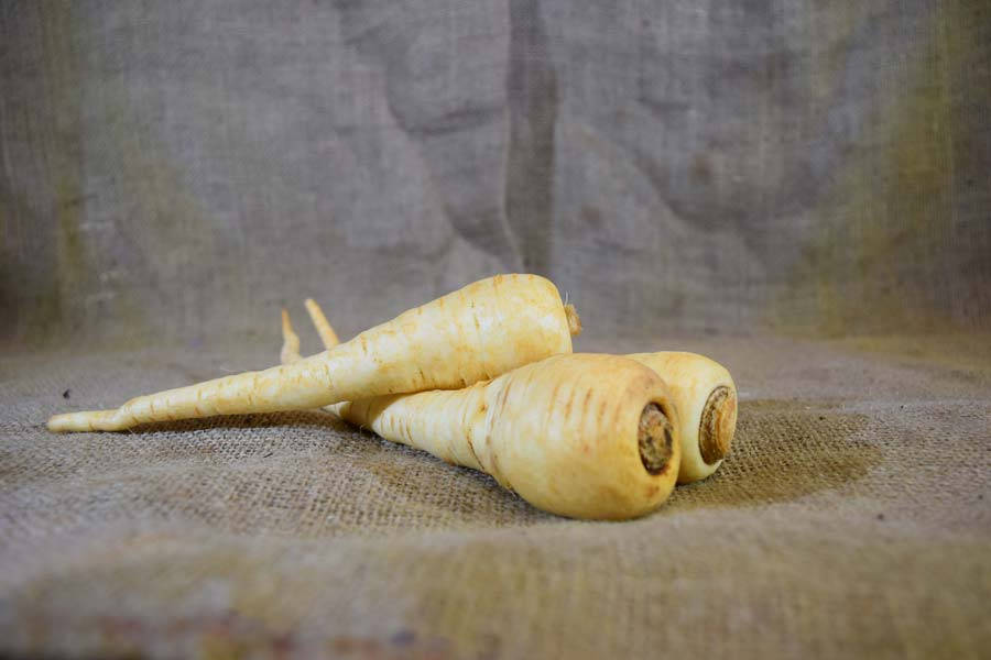 Parsnip 桌布 壁紙 — 三個淡黃色的歐洲防風草放在粗糙的麻布上，背景為柔和的灰色，光線柔和。