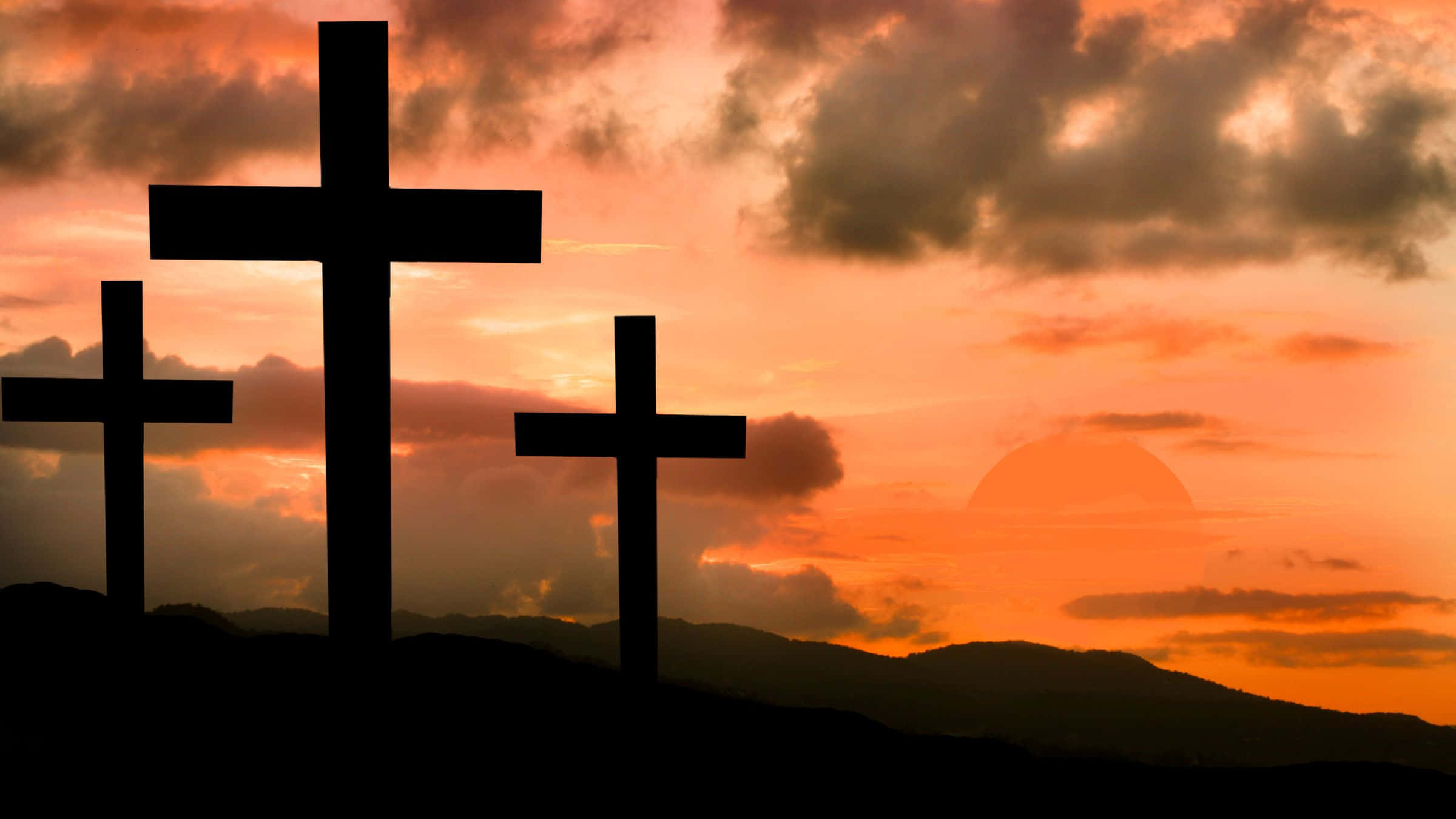 Good Friday 桌布 壁紙 — 三個深色十字架在火熱橙色日落天空的襯托下形成剪影，天空中有戲劇性的雲彩和遠處的山丘。