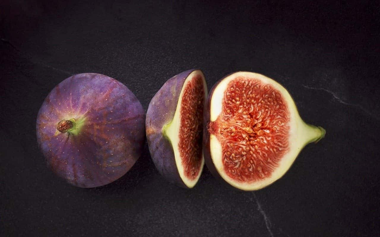 Purple Figs 桌布 壁紙 — 三個無花果，一個完整，兩個切半，露出多汁的紅色果肉，置於深色紋理表面上。