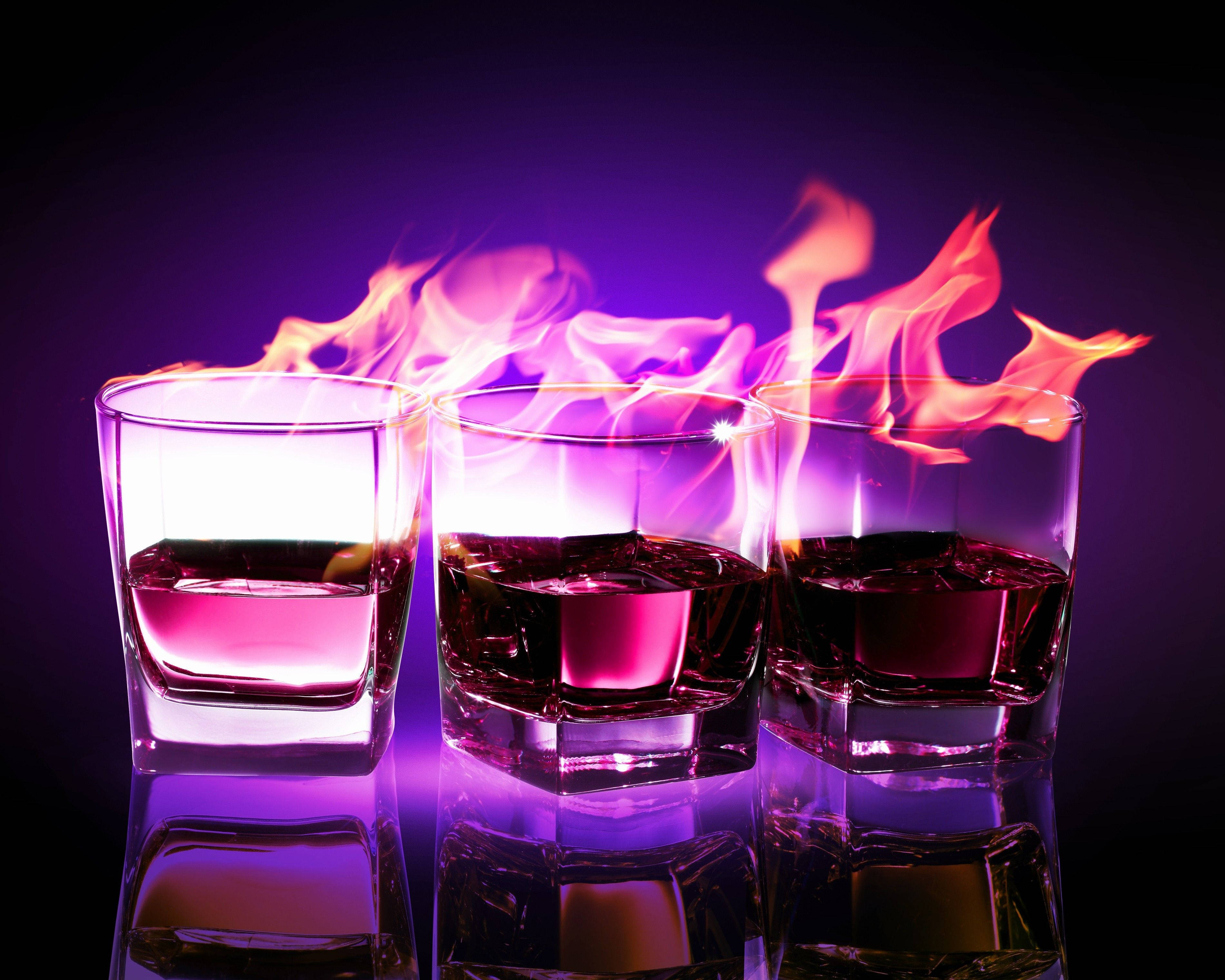 Drink 桌布 壁紙 — 三個燃燒的威士忌酒杯在黑暗背景下閃耀著鮮豔的紫色和橙色火焰。