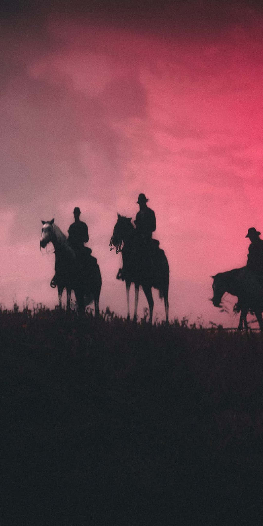 Red Dead Redemtion 2 桌布 壁紙 — 三個牛仔剪影騎馬穿過田野，背景是戲劇性的粉紅和紫色日落天空。