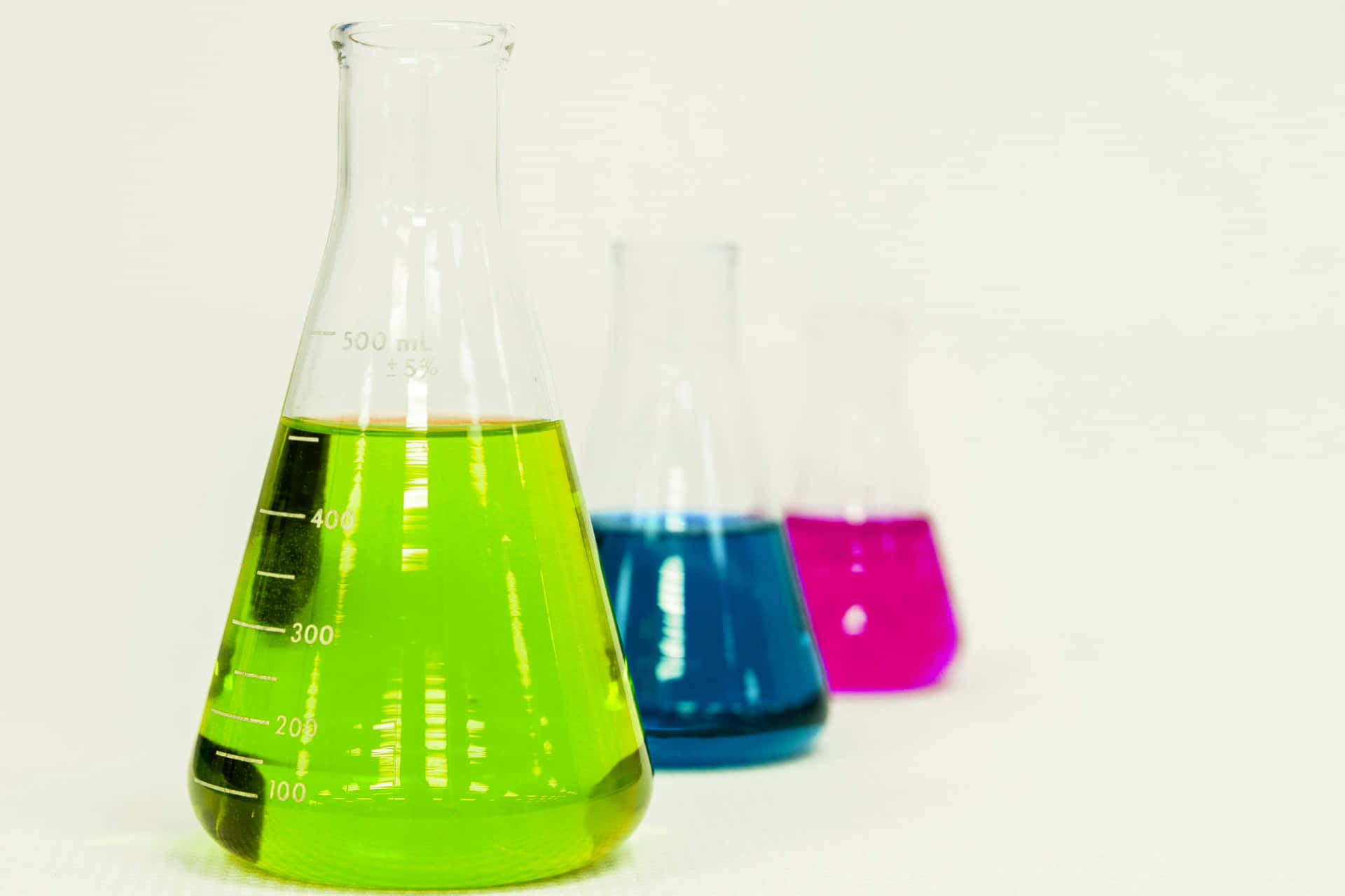 科學 桌布 壁紙 — 三個玻璃燒瓶裝滿充滿活力的綠色、藍色和洋紅色液體，在純白色背景上一字排開。
