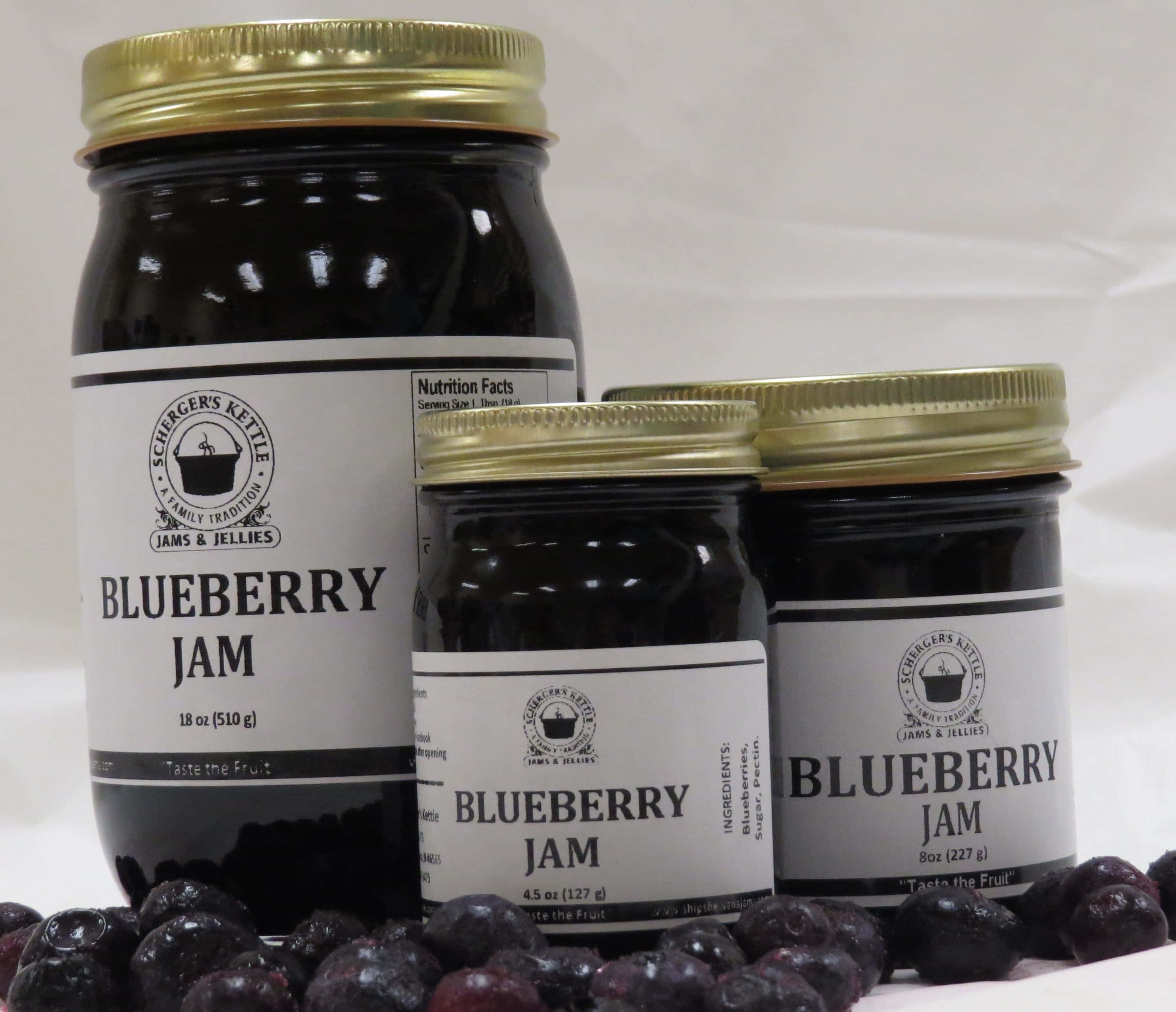 Blueberry Jam 桌布 壁紙 — 三個玻璃罐的藍莓果醬，配有金色蓋子和白色標籤，放在新鮮藍莓上，背景為純白色。