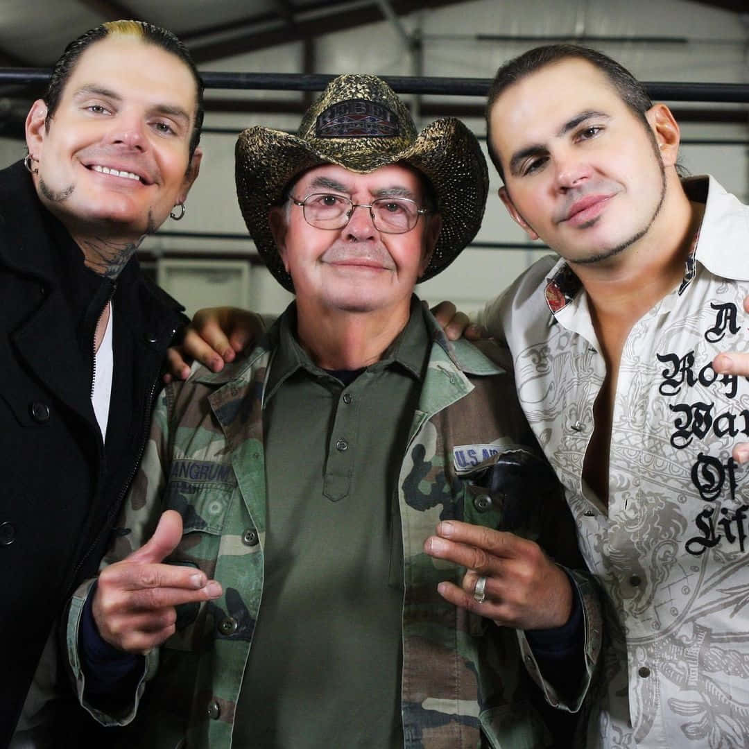 WWE 桌布 壁紙 — 三個男人在倉庫裡一起擺姿勢。一個戴著牛仔帽，另一個有刺青，第三個穿著圖案襯衫。