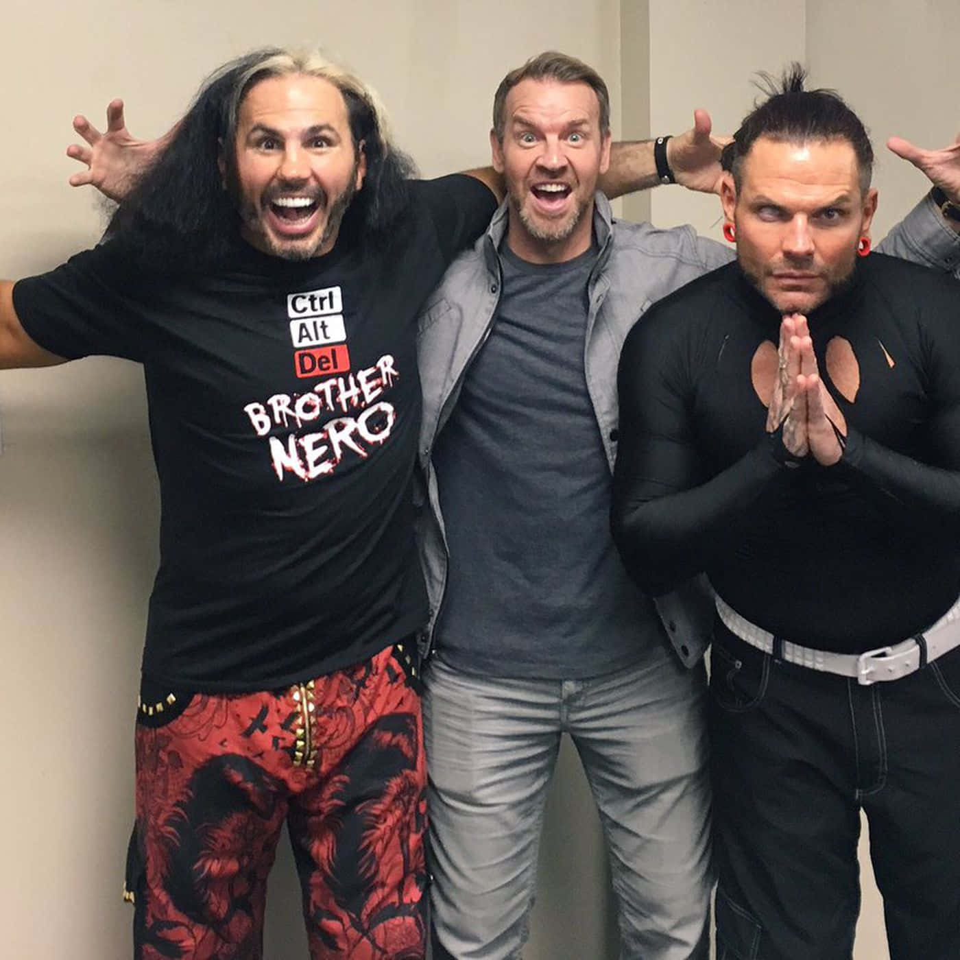 WWE 桌布 壁紙 — 三個男人在室內充滿活力地擺姿勢，一個尖叫，一個咧嘴笑，一個雙手合十，穿著大膽的服裝。