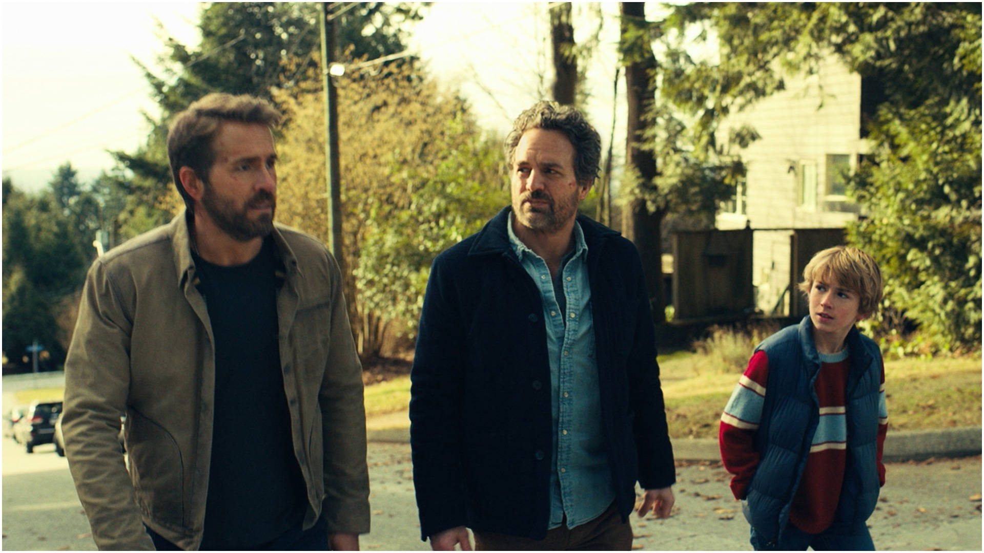 The Adam Project 桌布 壁紙 — 三個男人在溫暖的金色陽光下沿著綠樹成蔭的郊區街道行走，投下長長的影子。