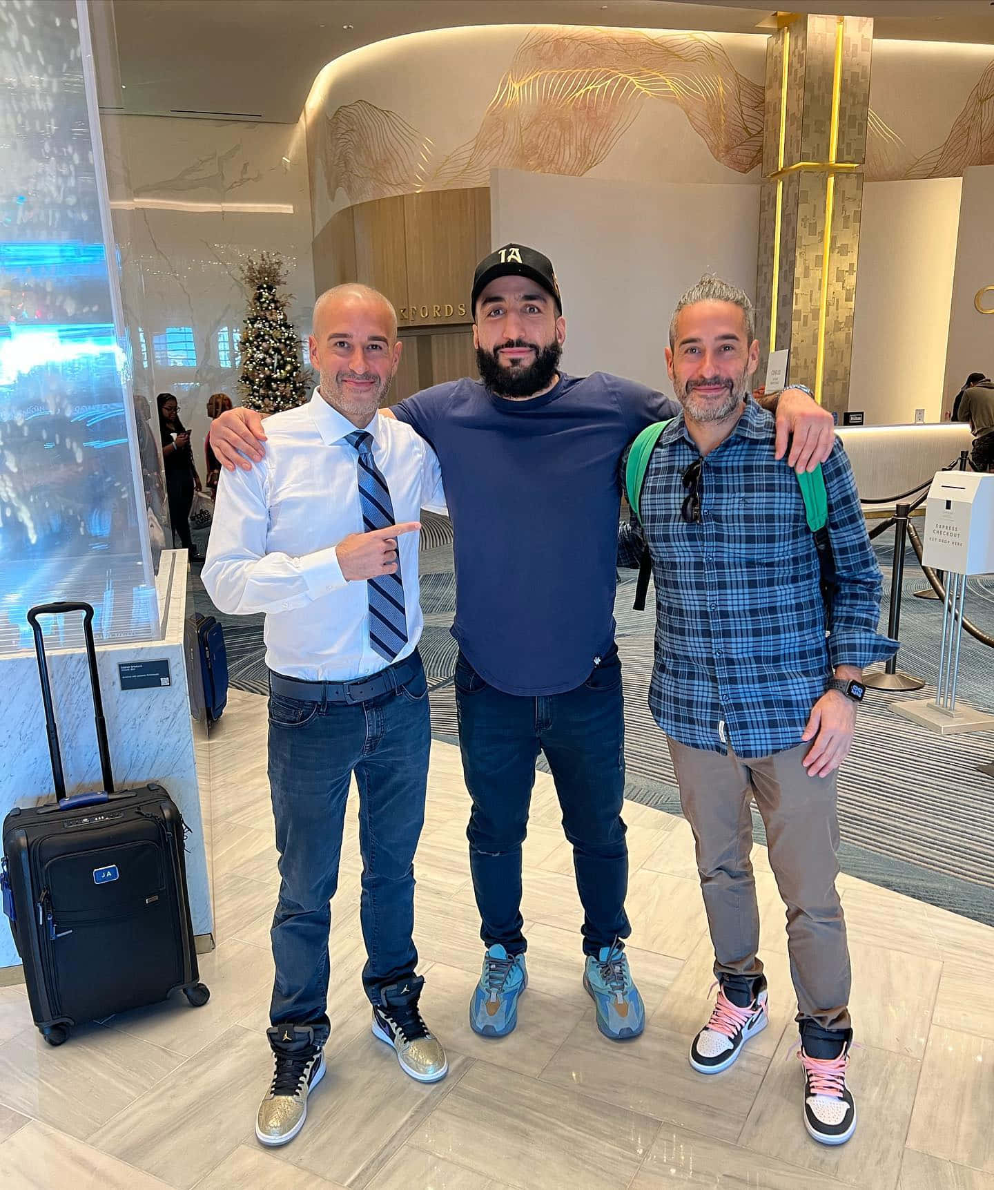 UFC 桌布 壁紙 — 三個男人在現代飯店大廳裡一起擺姿勢，旁邊有聖誕樹和行李。