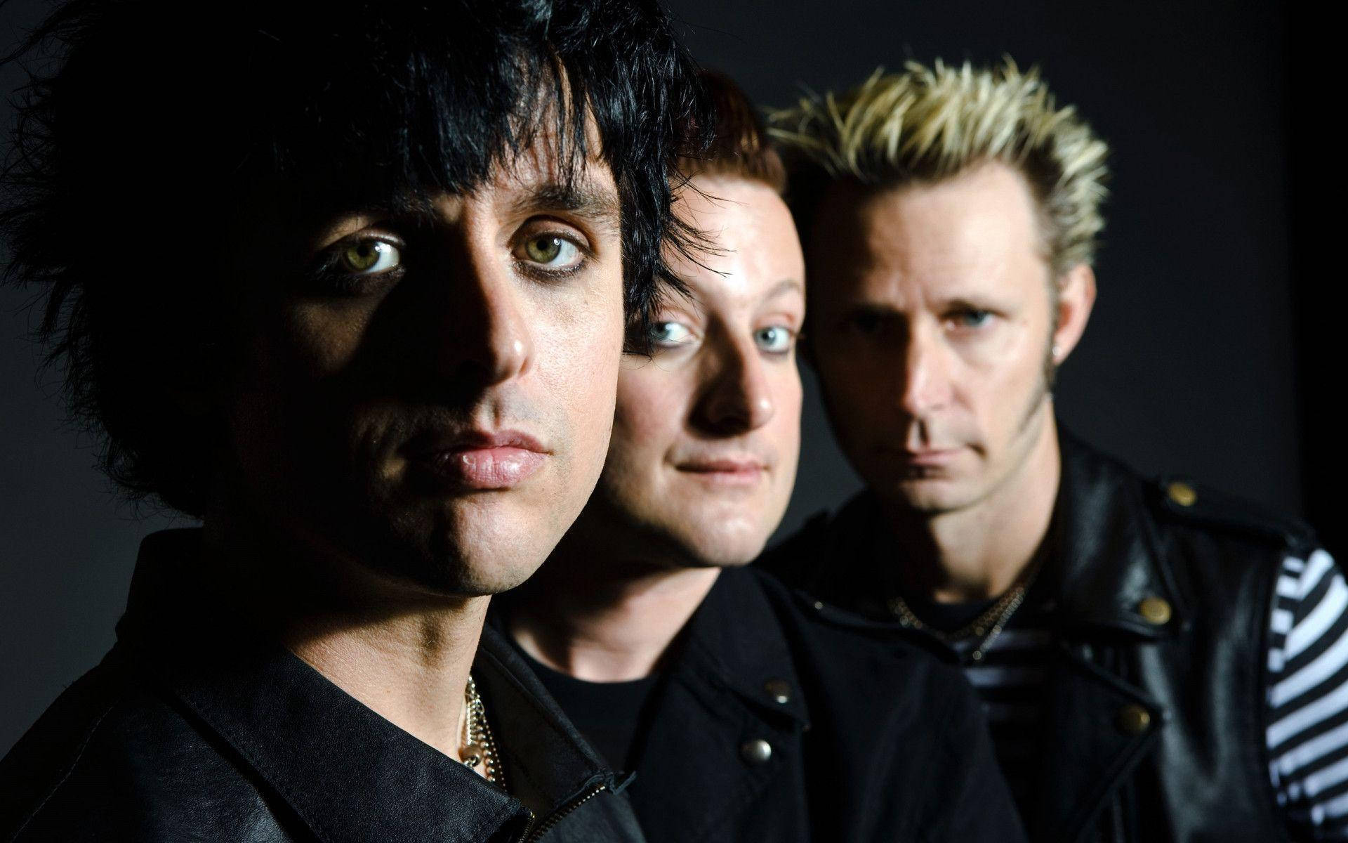 Green Day 桌布 壁紙 — 三個男人帶著強烈的目光和龐克風格的髮型，在黑暗背景下直視鏡頭。