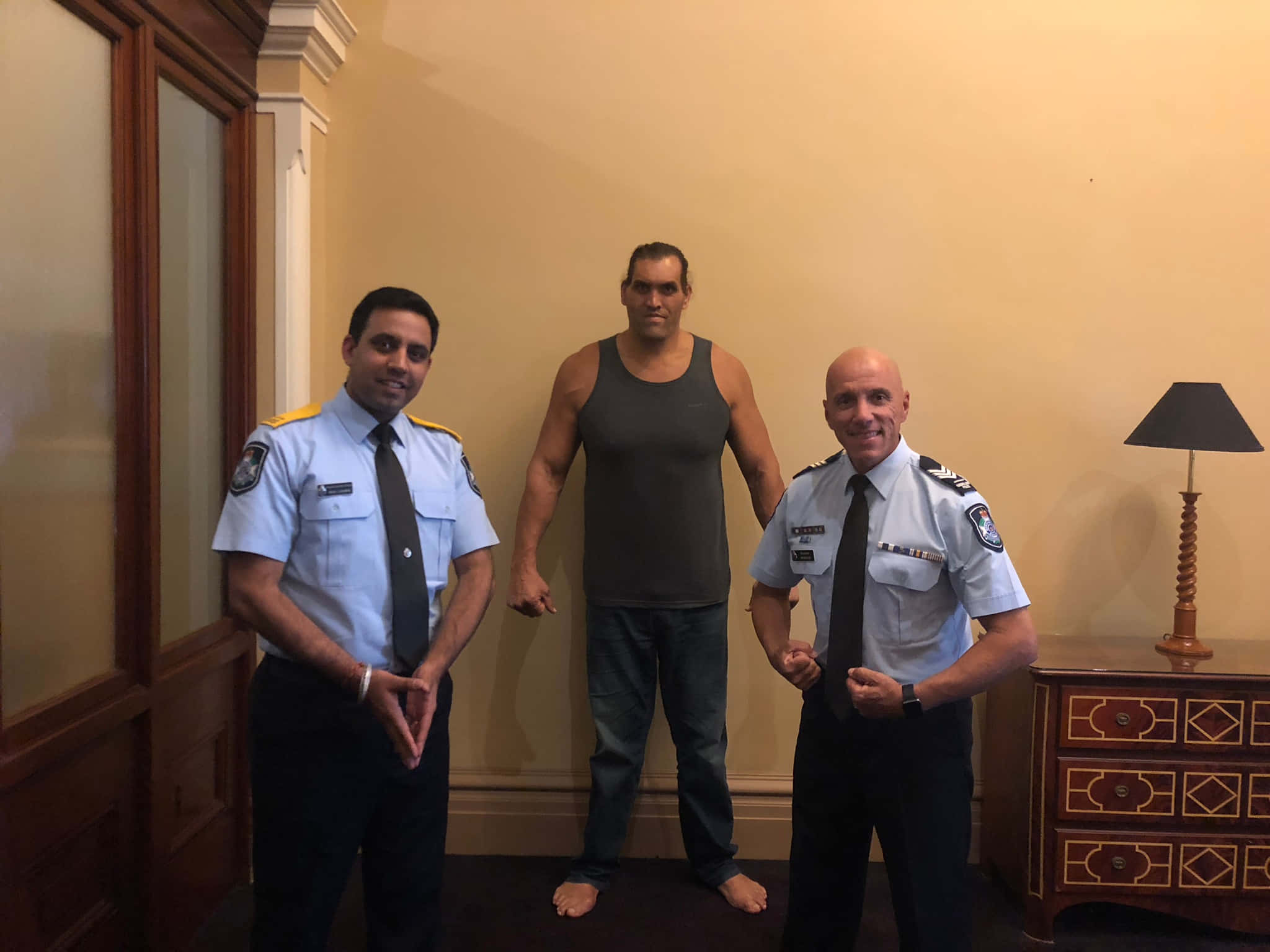 Indian 桌布 壁紙 — 三個男人站在一個溫暖照明的房間裡，兩個穿著警察制服的男人夾著一個穿著背心的肌肉男。