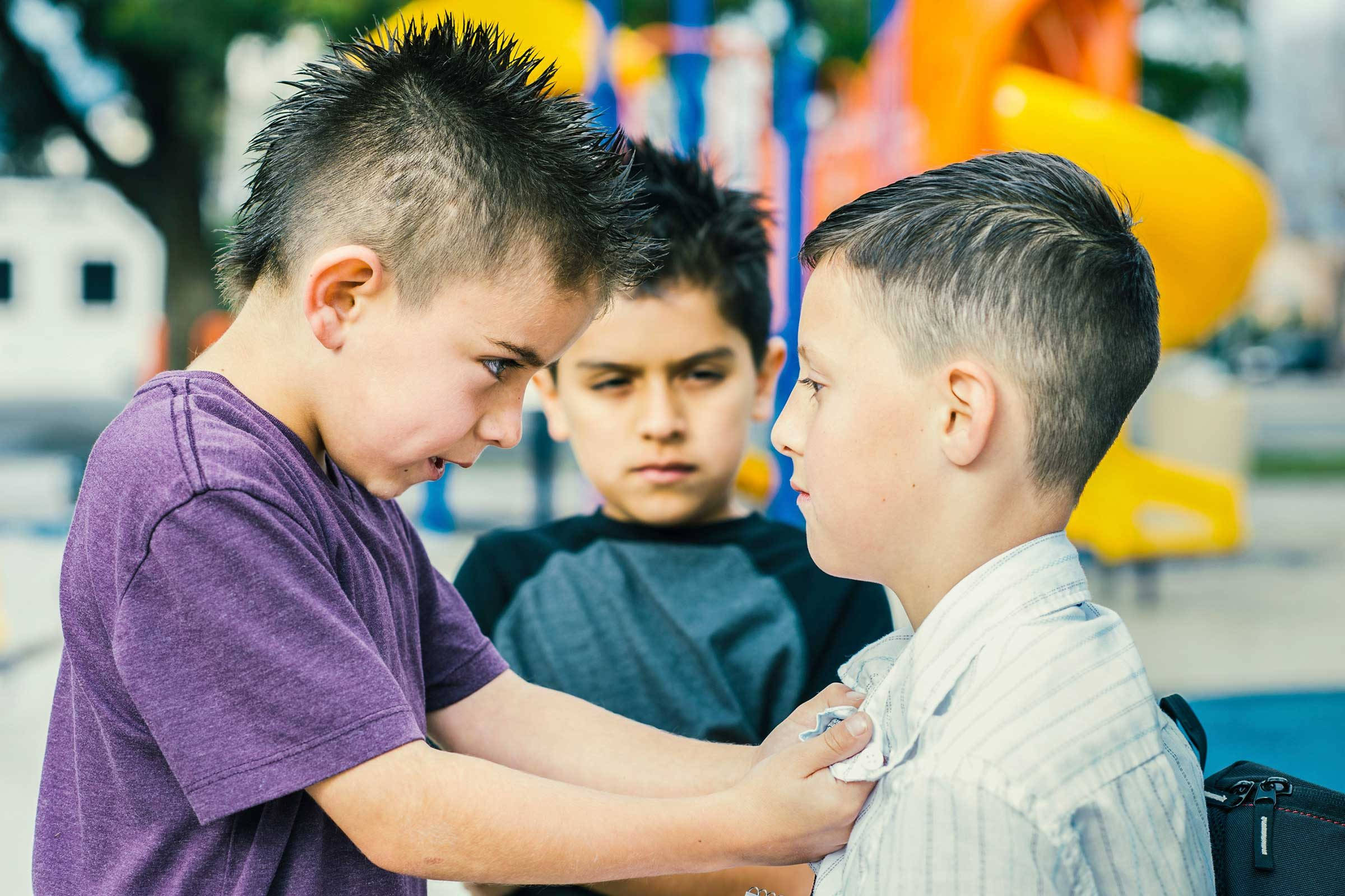 rude 桌布 壁紙 — 三個男孩在遊樂場，一個安慰另一個，而第三個在柔和日光下專注地觀看。