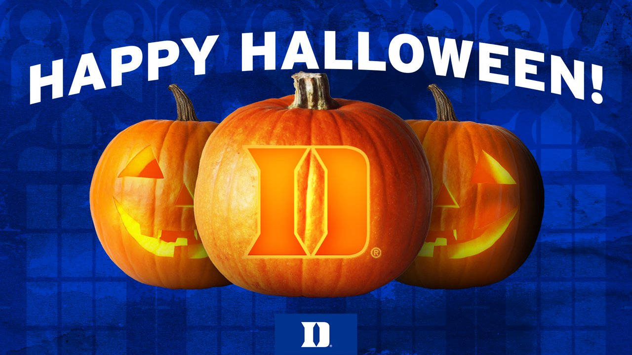 Duke Blue Devils 桌布 壁紙 — 三個發光的傑克南瓜燈，中間的南瓜雕刻有杜克大學標誌，背景為深藍色圖案，並帶有「HAPPY HALLOWEEN!」文字。