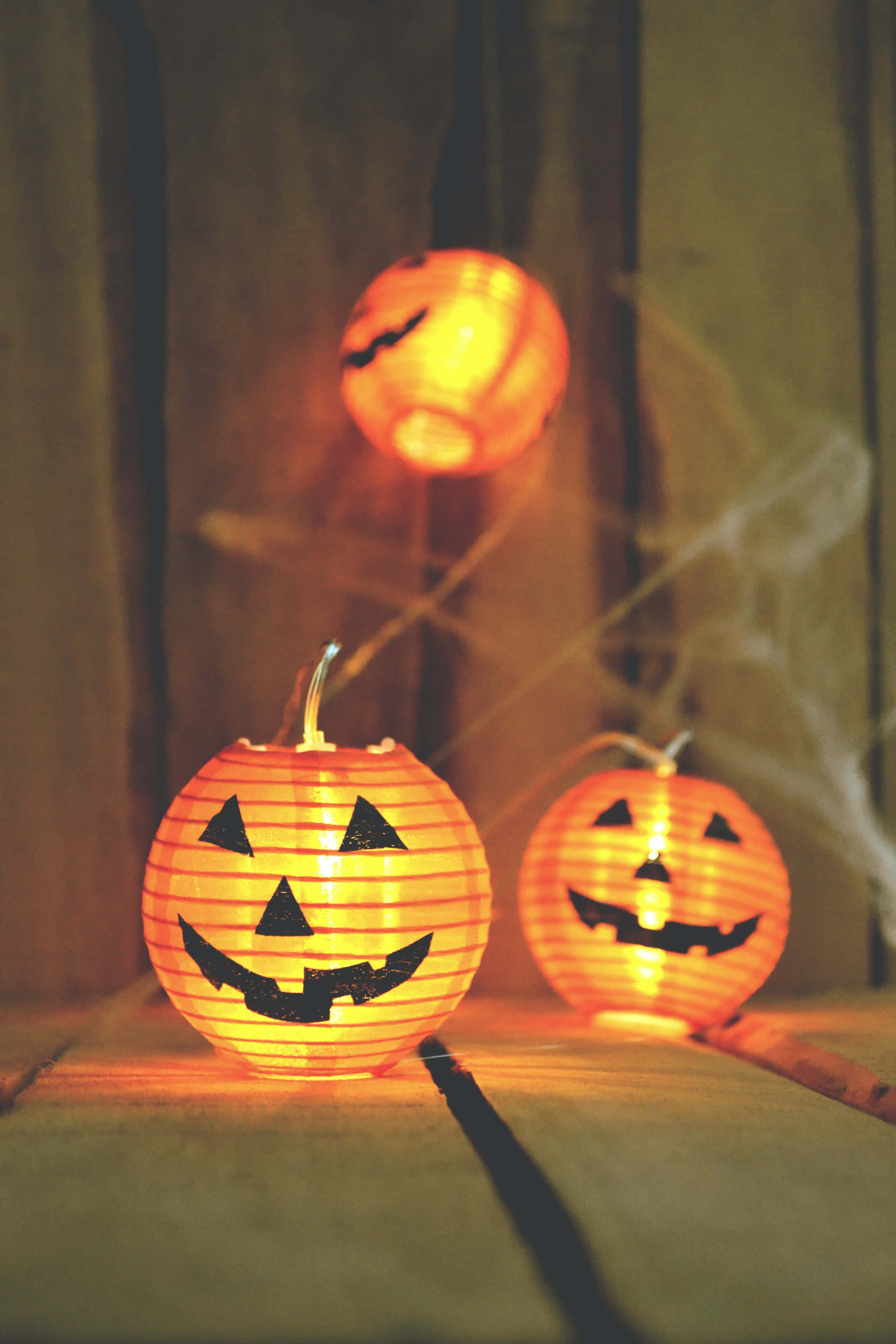 jack o'lantern 桌布 壁紙 — 三個發光的傑克南瓜燈籠，帶有黑色三角形面孔，在木質表面上投射溫暖的光芒，周圍有輕煙飄散。