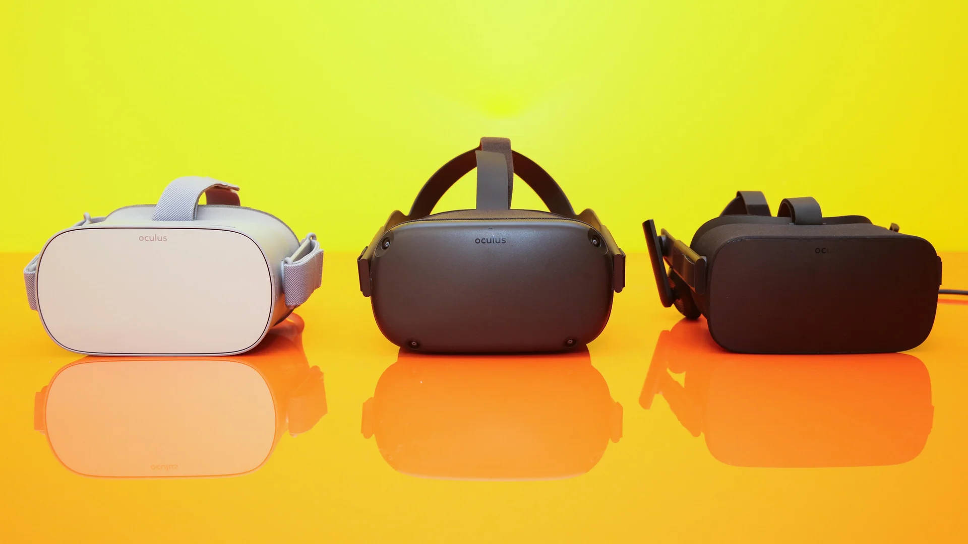 Quest 桌布 壁紙 — 三個白色、灰色和黑色的 Oculus VR 頭戴式裝置放在光滑的橙色表面上，背景為明亮的黃色。