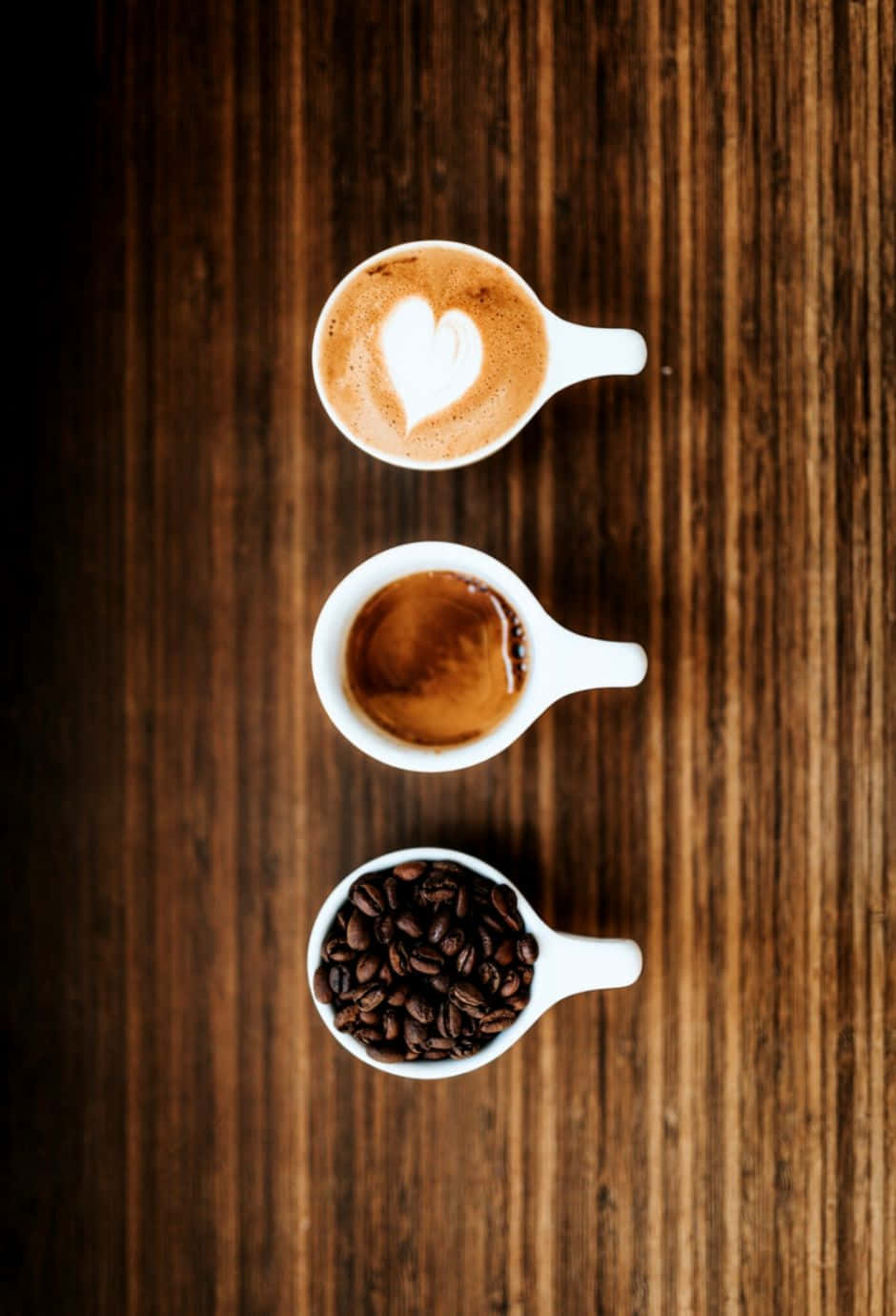 Black Coffee 桌布 壁紙 — 三個白色杯子在木上一字排開：帶心形奶泡的拿鐵、濃縮咖啡和烘焙咖啡豆。