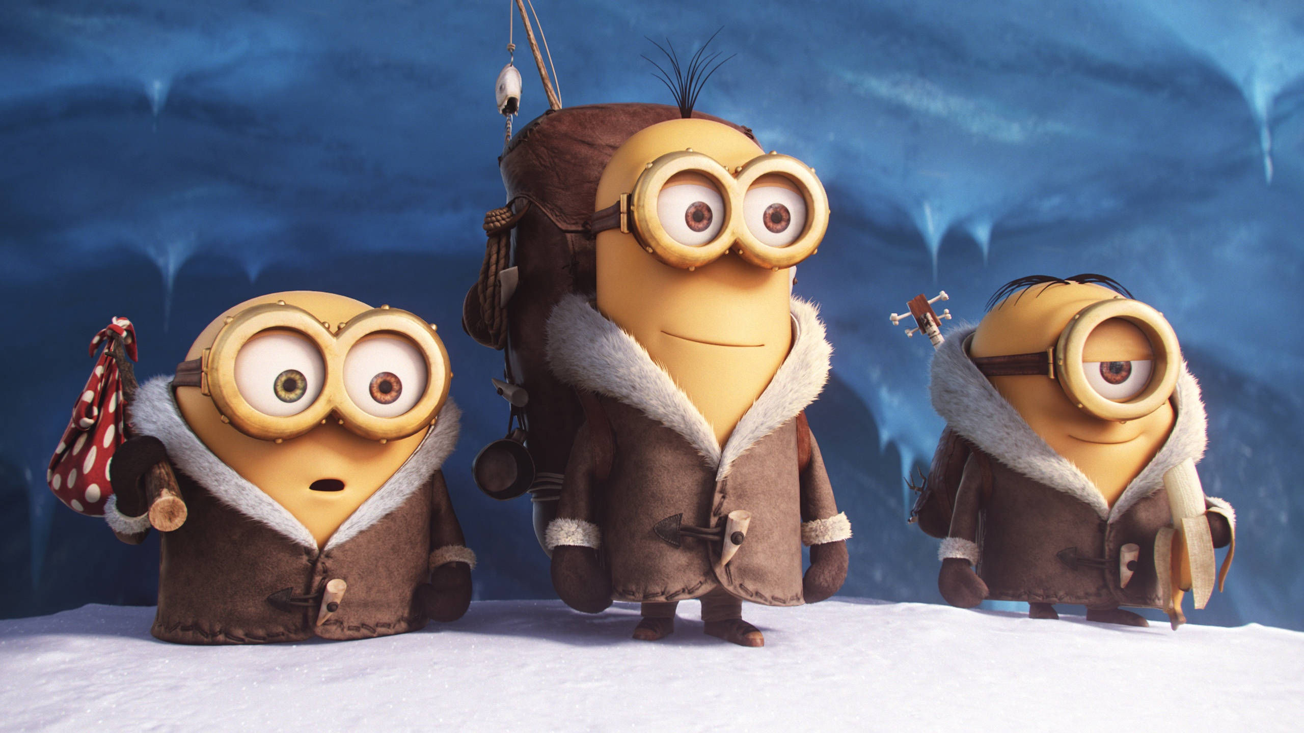 minions the rise of gru 桌布 壁紙 — 三個穿著冬季外套的小小兵站在一個有冰藍色牆壁和懸掛冰柱的雪洞中。