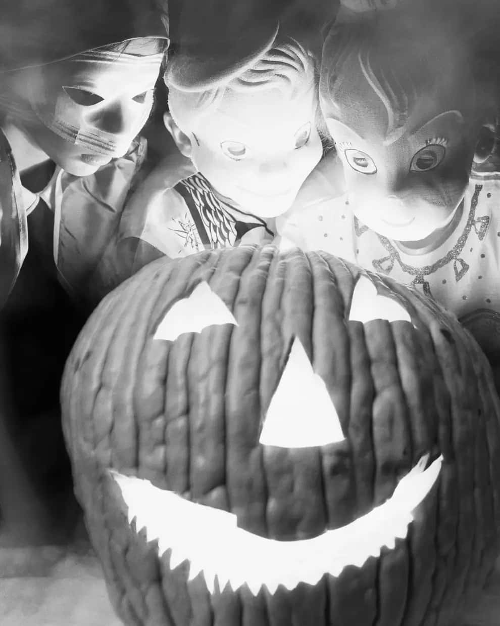Creepy Halloween 桌布 壁紙 — 三個穿著復古萬聖節服裝的孩子好奇地凝視著一個發光的傑克南瓜燈，它露出寬闊的牙齒笑容。