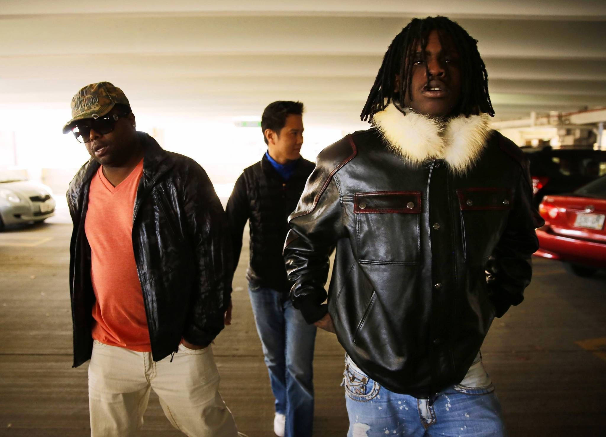 Chief Keef 桌布 壁紙 — 三個穿著皮夾克的男人穿過一個燈光昏暗的停車場，周圍停著汽車。