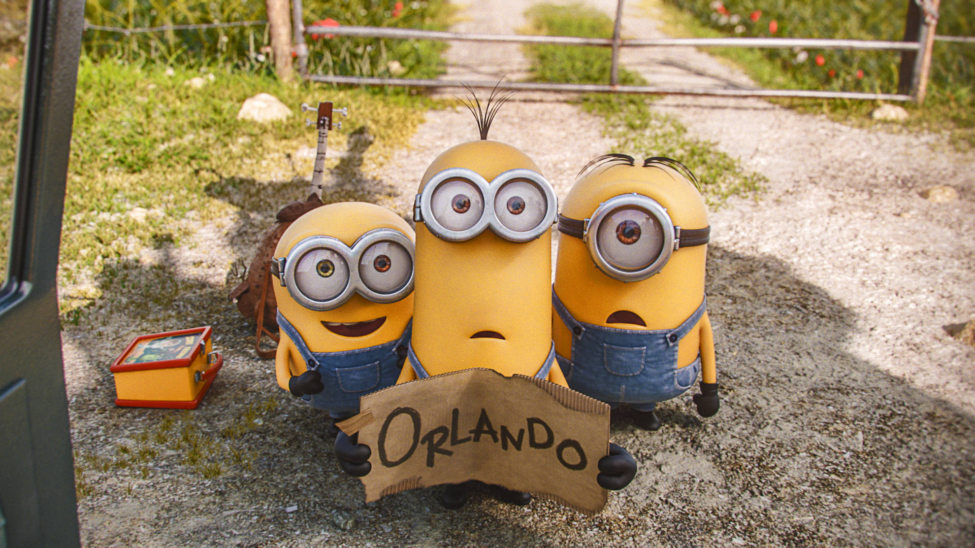minions the rise of gru 桌布 壁紙 — 三個穿著藍色吊帶褲的黃色小小兵在圍籬附近的碎石路上舉著寫有Orlando的紙板標牌。