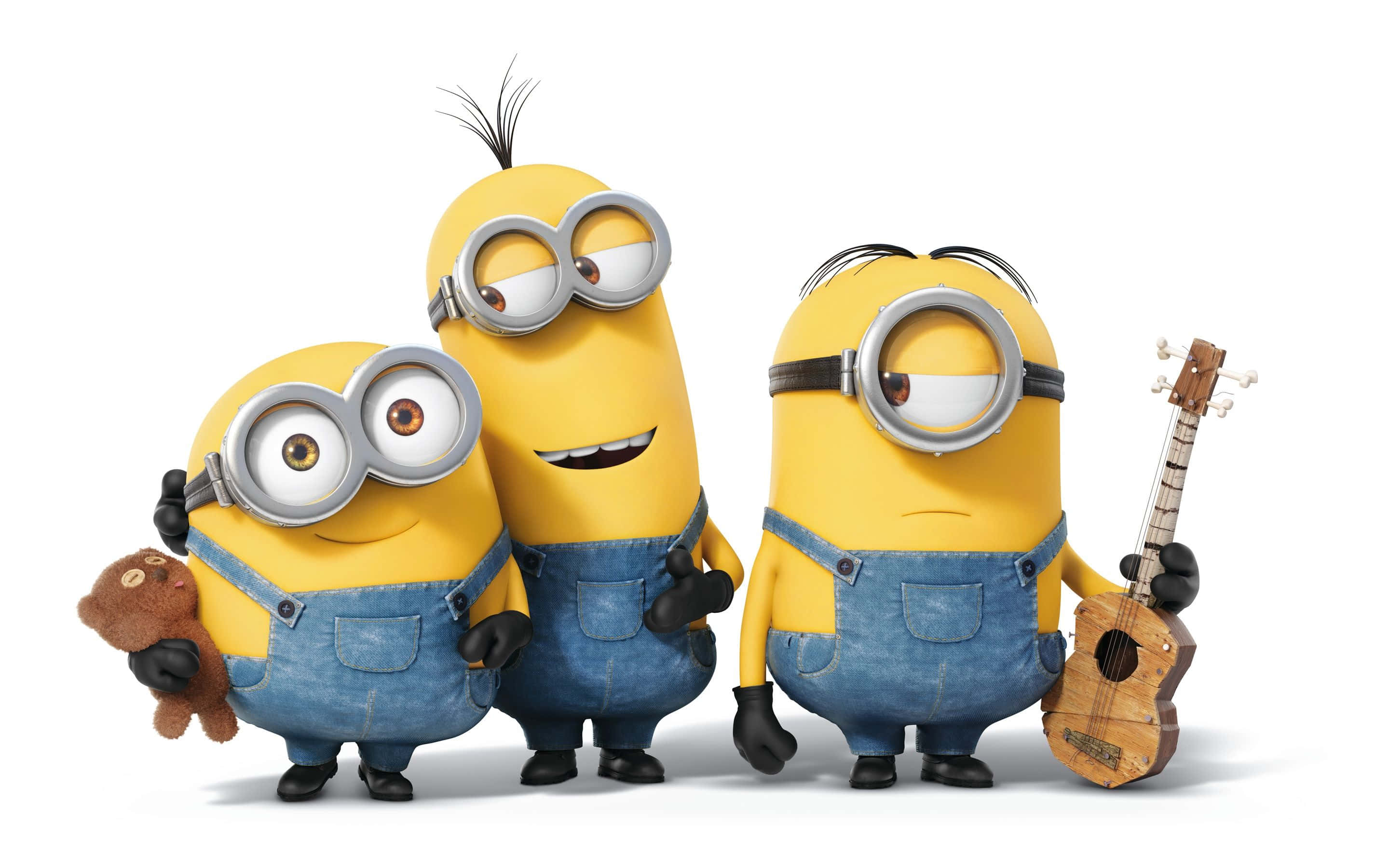 小黃人 桌布 壁紙 — 三個穿著藍色工裝褲的開心黃色Minions，在純白色背景前與一隻泰迪熊和烏克麗麗擺姿勢。