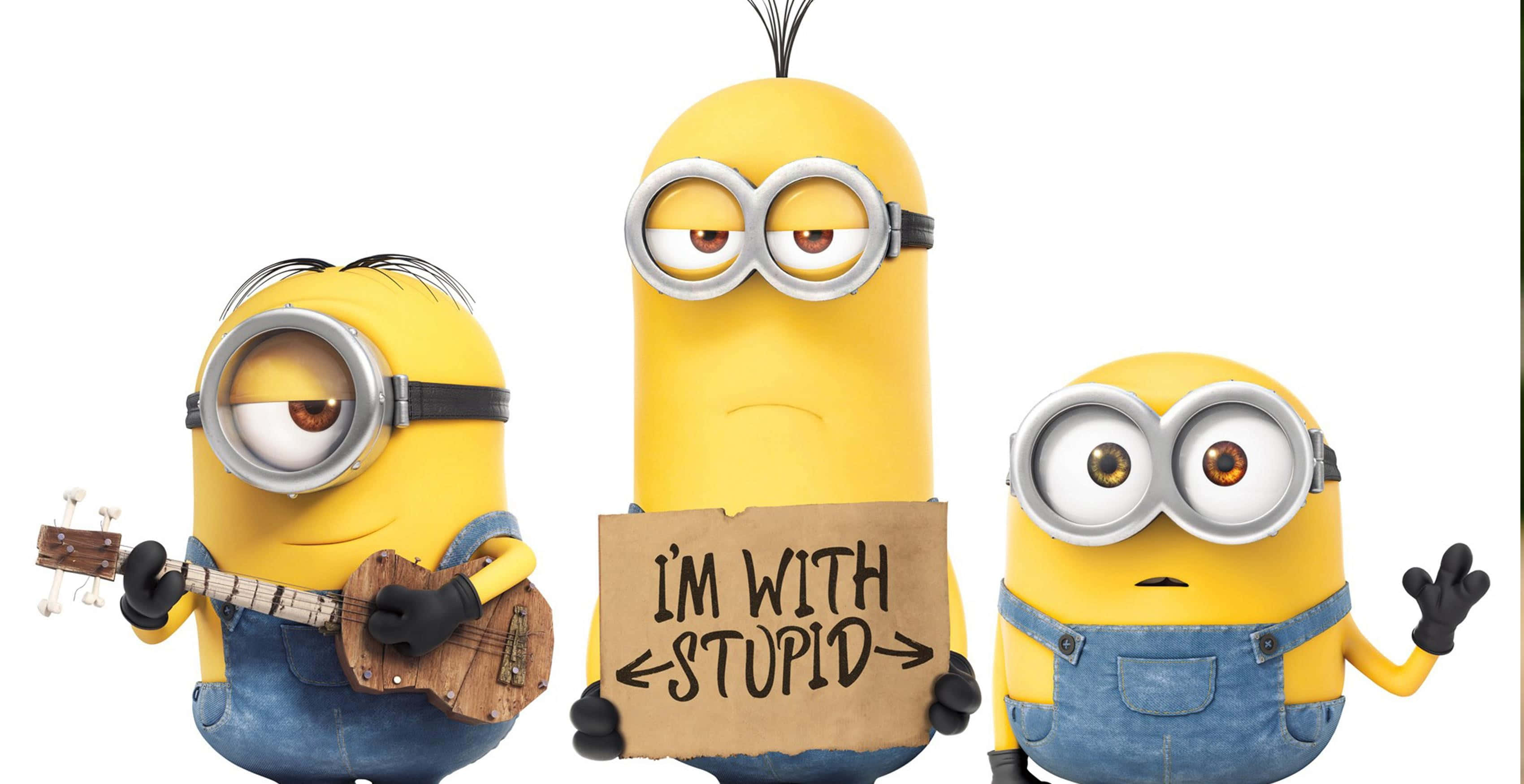 桌布 壁紙 — 三個穿著藍色工裝褲的黃色Minions，一個彈奏烏克麗麗，一個舉著寫有I'M WITH STUPID的牌子，一個在白色背景前開心地揮手。