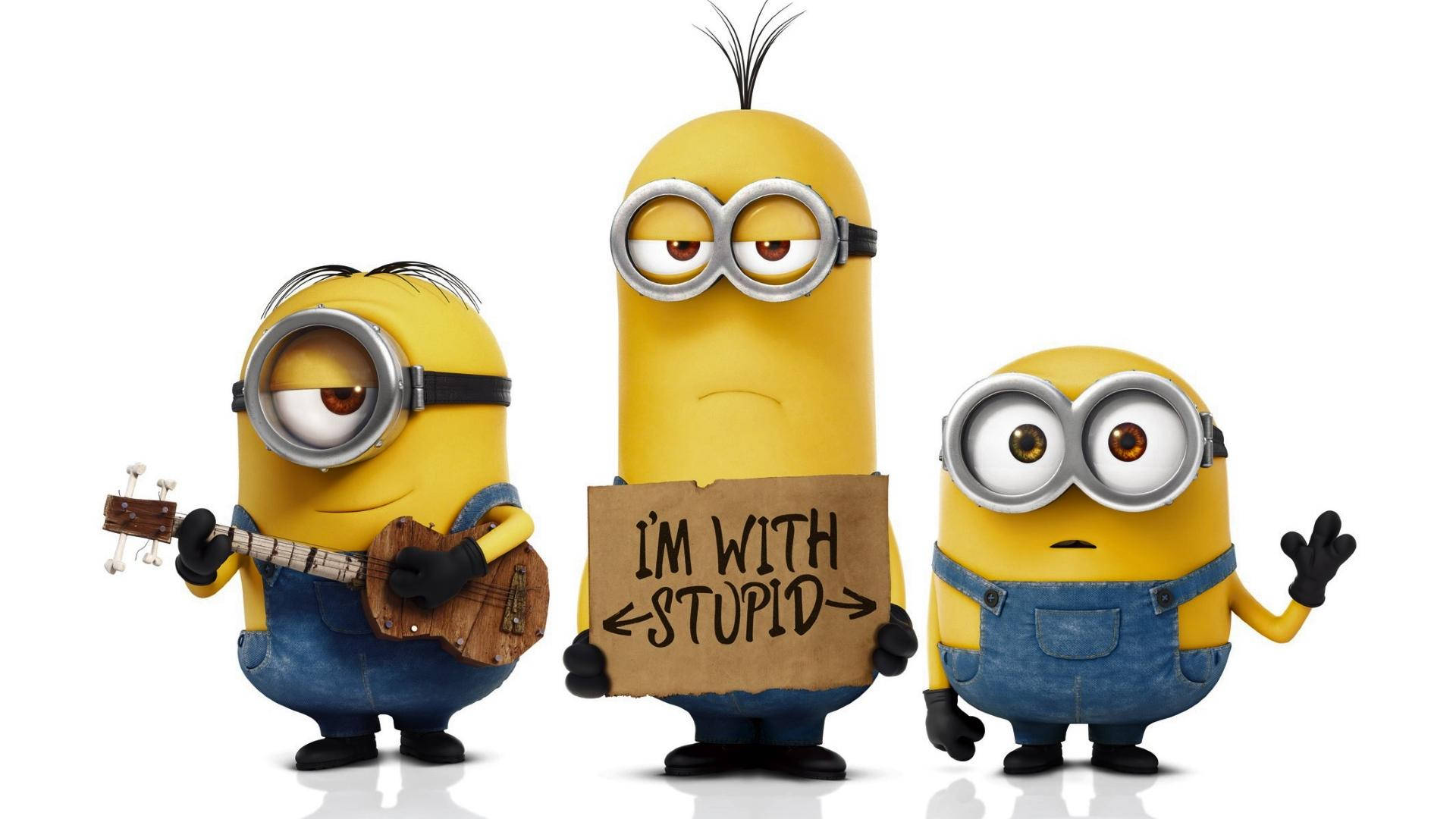 1080p HD 桌布 壁紙 — 三個穿著藍色工裝褲的黃色Minions開心擺姿勢，一個彈奏烏克麗麗，一個舉著寫有I'M WITH STUPID的牌子，背景為白色。