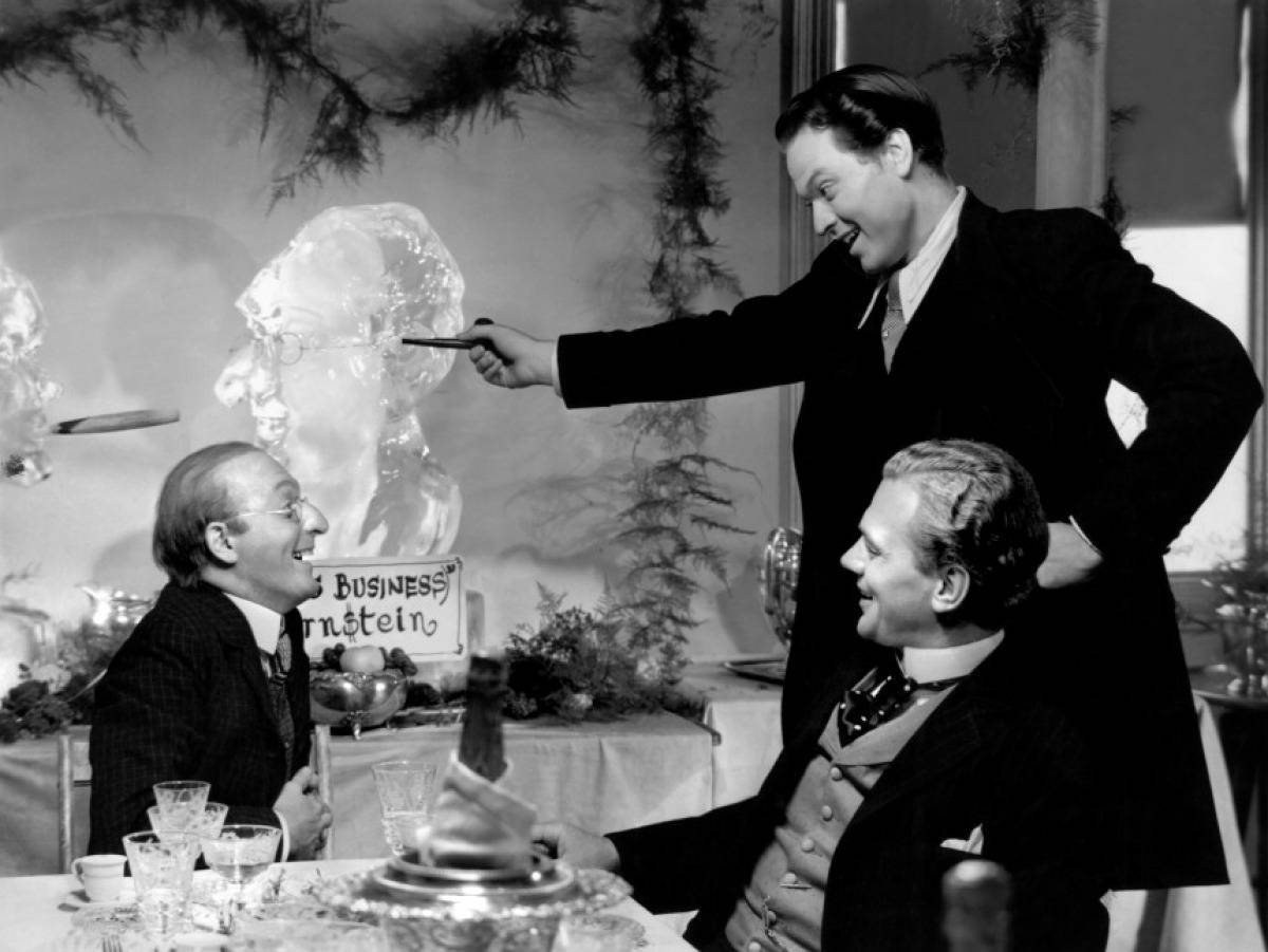 Citizen Kane 桌布 壁紙 — 三個穿著西裝的男人圍著桌子大笑，其中一個指著一個冰雕面孔，場景是復古黑白。