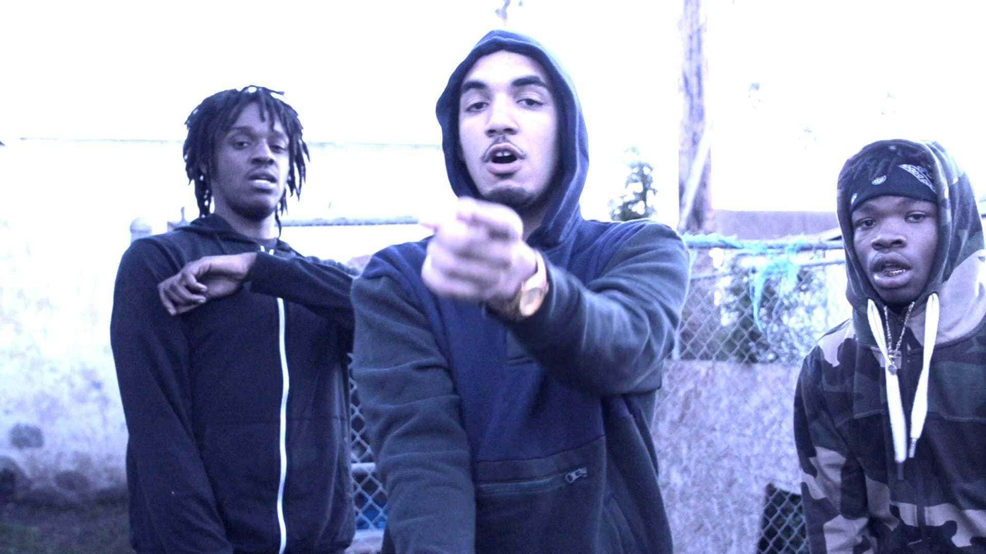 Shoreline Mafia 桌布 壁紙 — 三個穿著連帽衫的年輕男子在戶外強烈擺姿勢，其中一人向前指著，在冷藍色調下。