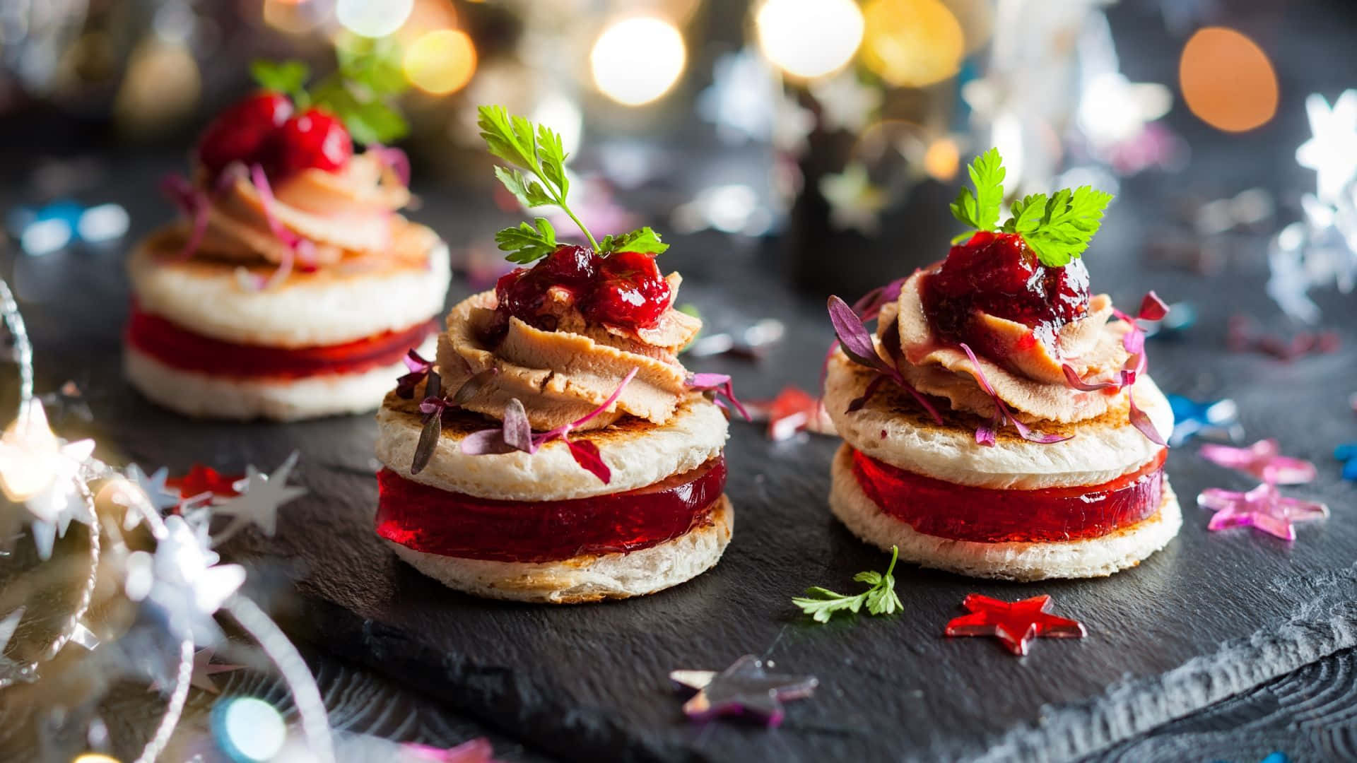 Desserts 桌布 壁紙 — 三個節日迷你三明治配蔓越莓醬和香草，放在深色石板板上，周圍有閃爍的燈光和星星紙屑。