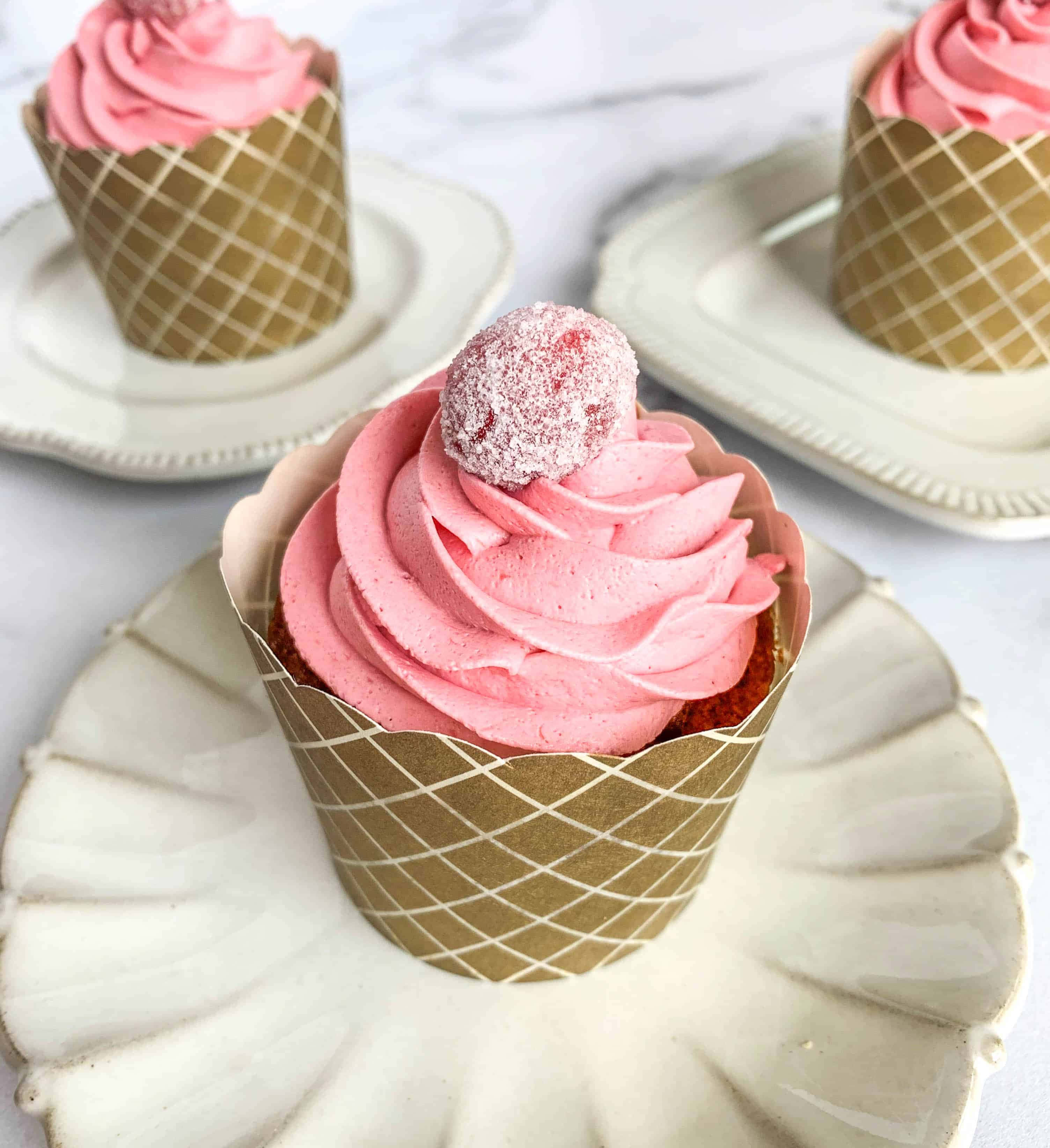 Pink Cupcakes 桌布 壁紙 — 三個粉紅色糖霜杯子蛋糕放在金色格子襯紙中，優雅地置於白色扇貝邊盤子上，背景為大理石。