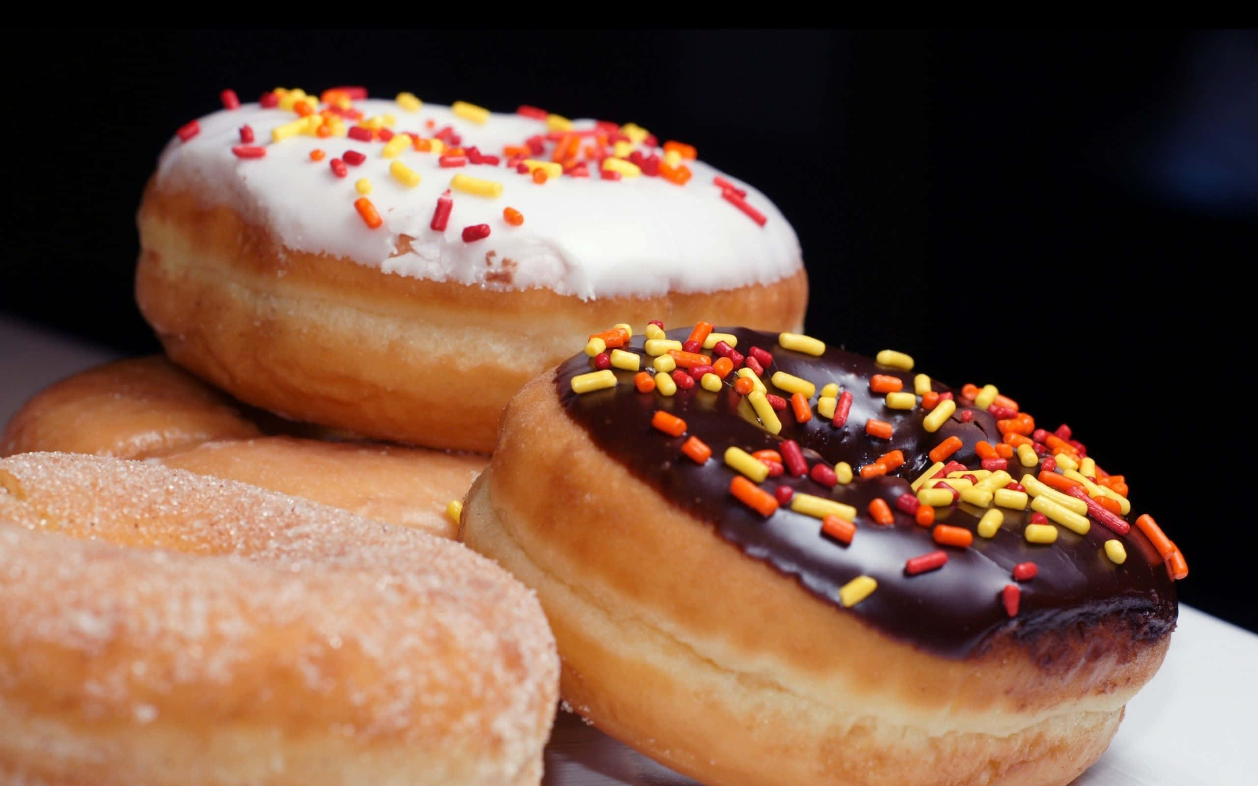 donuts 桌布 壁紙 — 三個糖霜彩針甜甜圈疊放在白色盤子上，背景深色。