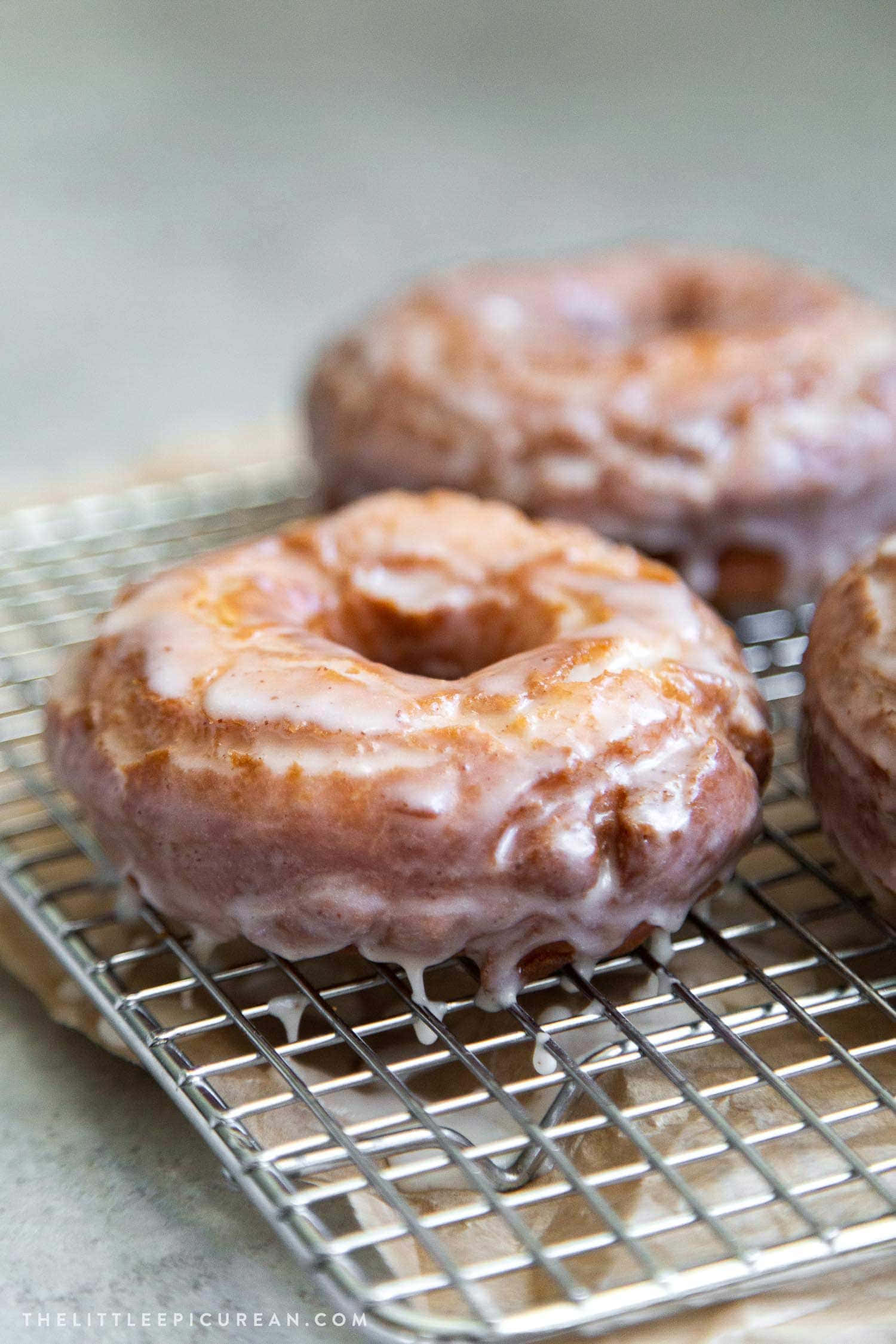 Glazed Donut 桌布 壁紙 — 三個糖霜肉桂甜甜圈放在金屬冷卻架上，閃亮的糖霜沿著側邊滴落。