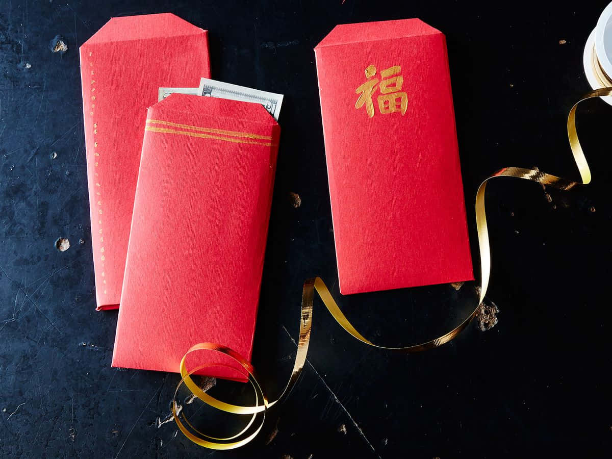 Red Envelope 桌布 壁紙 — 三個紅色中式紅包，金色邊框，其中一個印有「福」字，放在深色紋理表面上，旁邊有一條金色絲帶。
