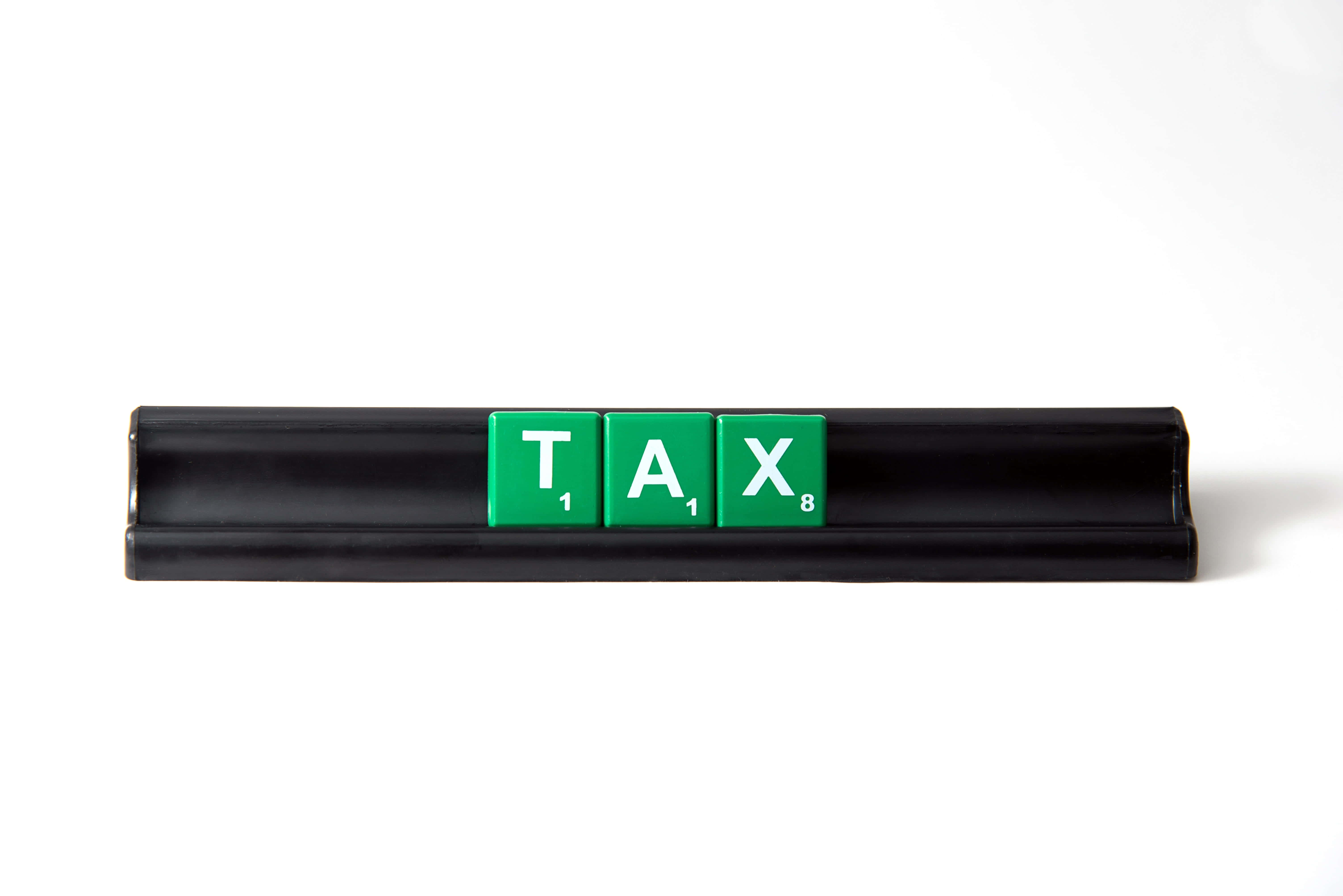 Educational Games 桌布 壁紙 — 三個綠色 Scrabble 字母牌拼出 TAX，放在黑色長方形底座上，背景為純白色。