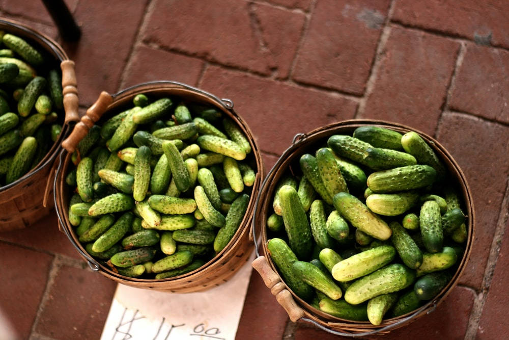 Pickle 桌布 壁紙 — 三個編織籃子裝滿新鮮青瓜酸菜，放在紅磚人行道上，附有手寫價格標籤。