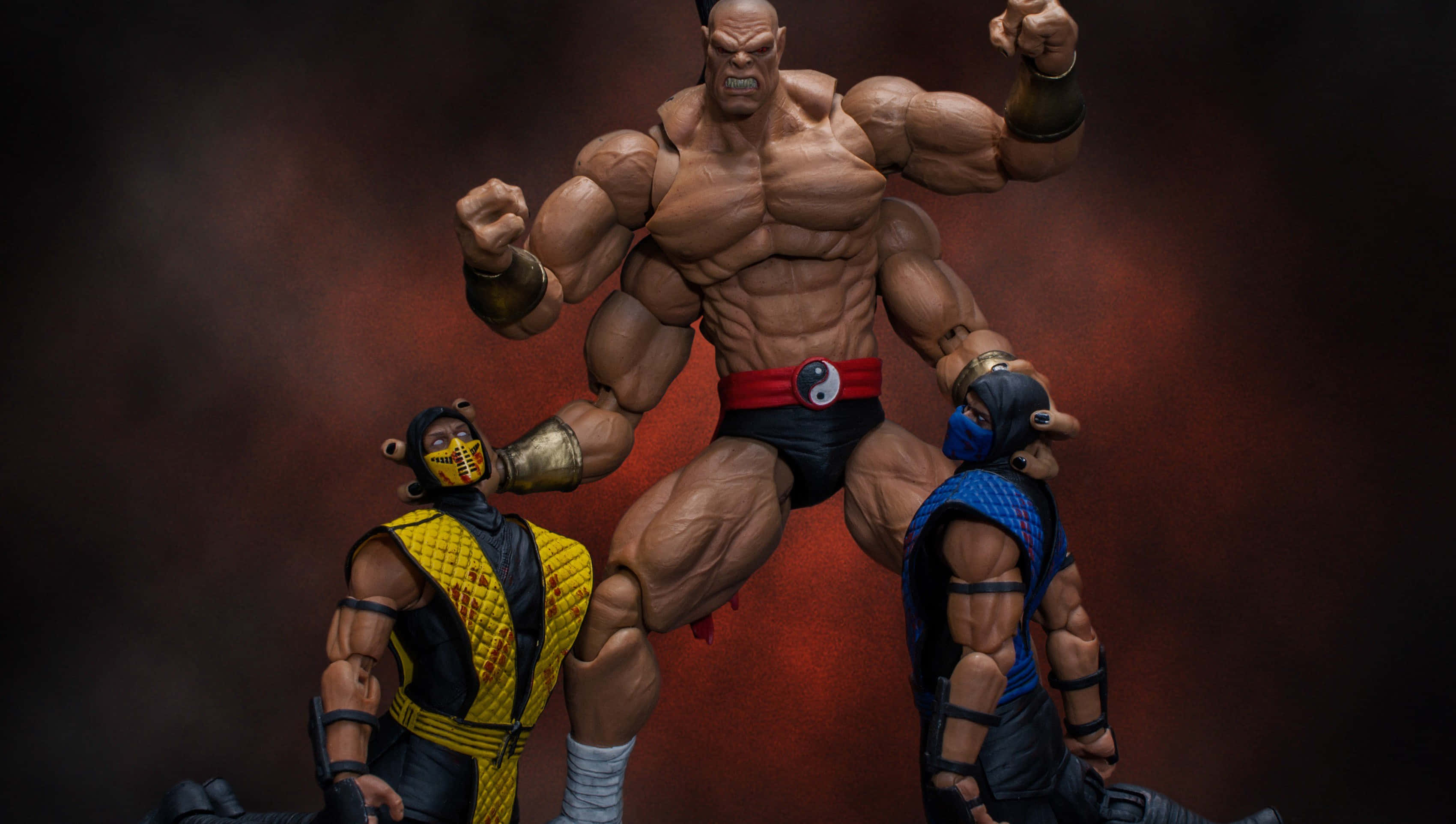Mortal Kombat Goro 桌布 壁紙 — 三個肌肉發達的真人快打動作人偶在煙霧瀰漫的紅色背景下動態擺姿勢。