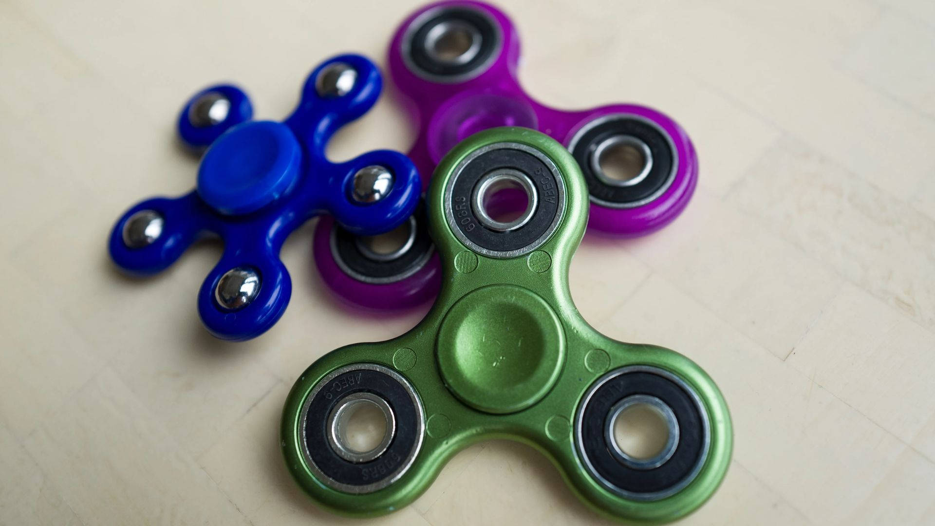 toys 桌布 壁紙 — 三個色彩繽紛的指尖陀螺藍色紫色和綠色放在淺色木質表面上。